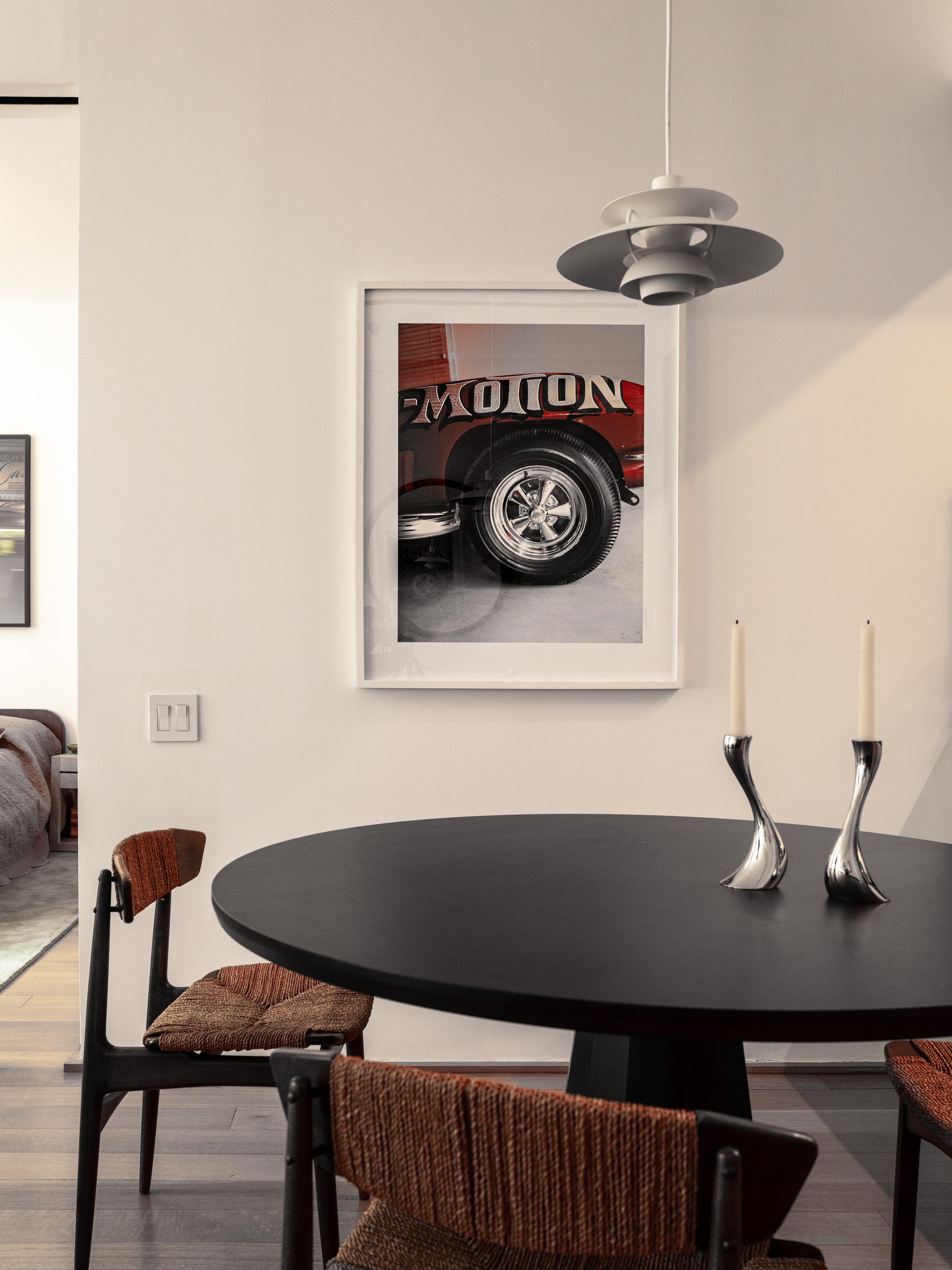 Dining area with sculptural pendant light, black round table, woven chairs, and framed wall artwork