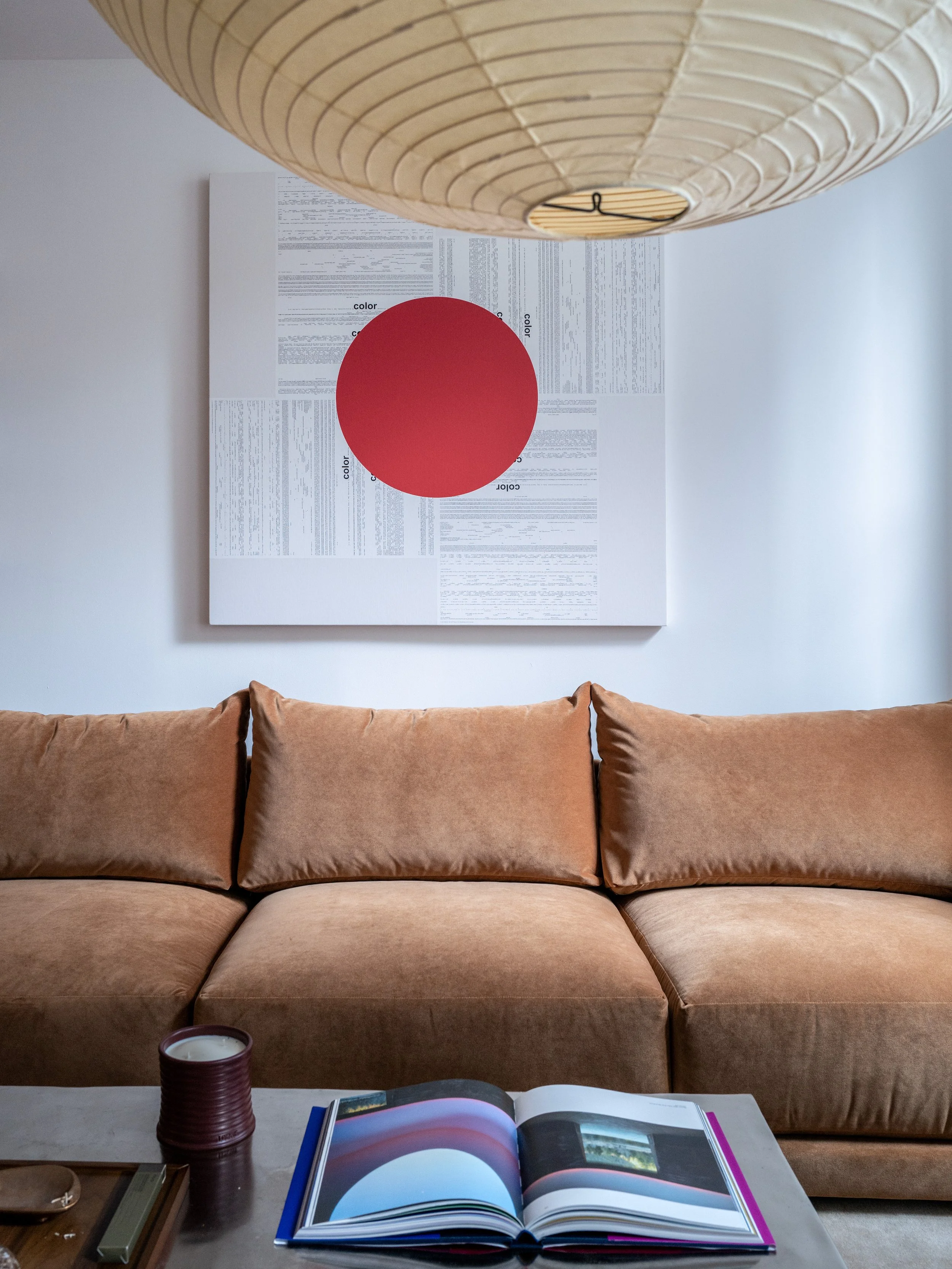 Sofa detail with velvet upholstery, large red circle canvas art, and paper globe pendant overhead