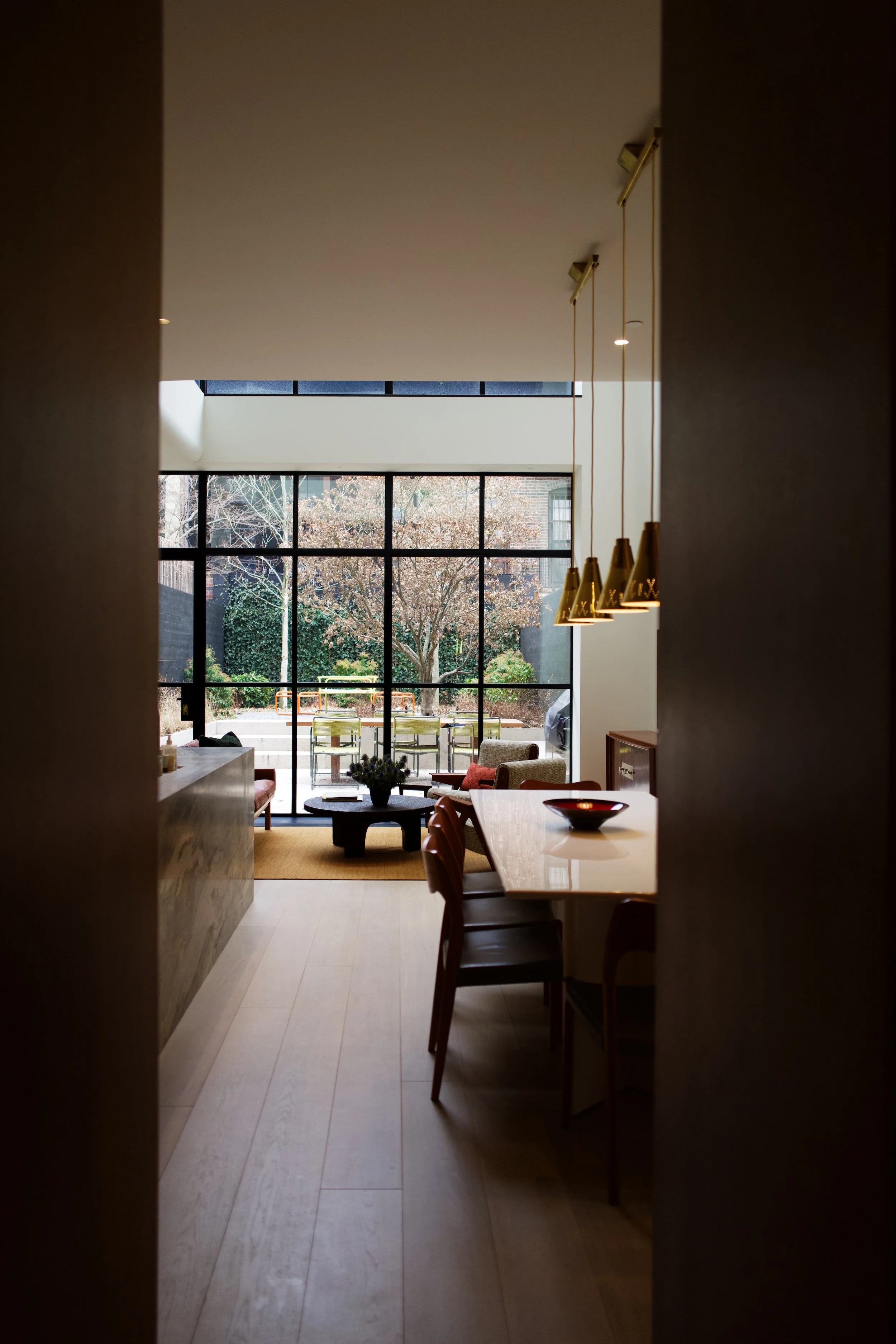 View through a dark threshold toward the living and dining area in a West Village townhouse by JG Neukomm Architecture