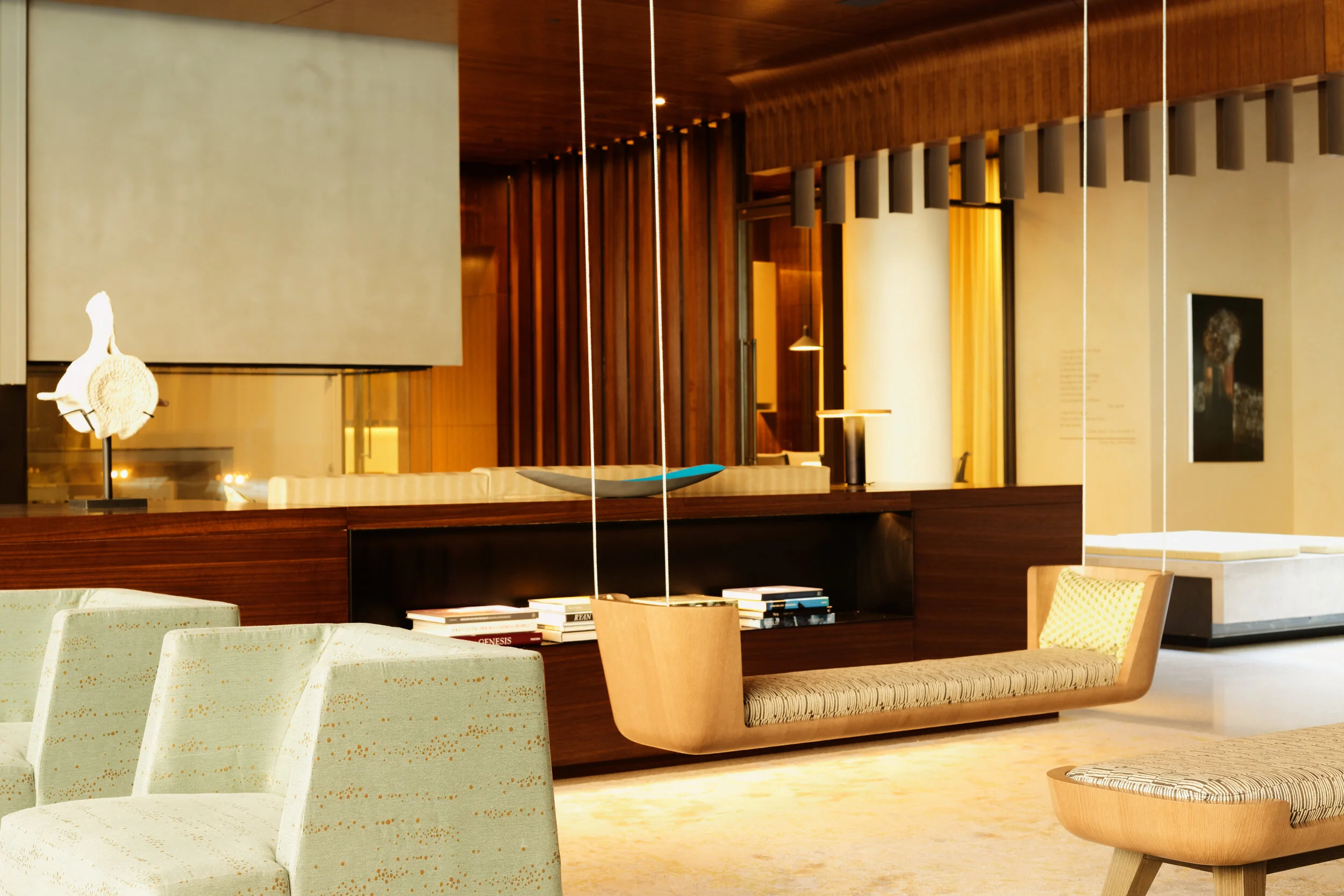 JGNA residential lounge with walnut paneling, suspended seating, an artwork display, and warm lighting