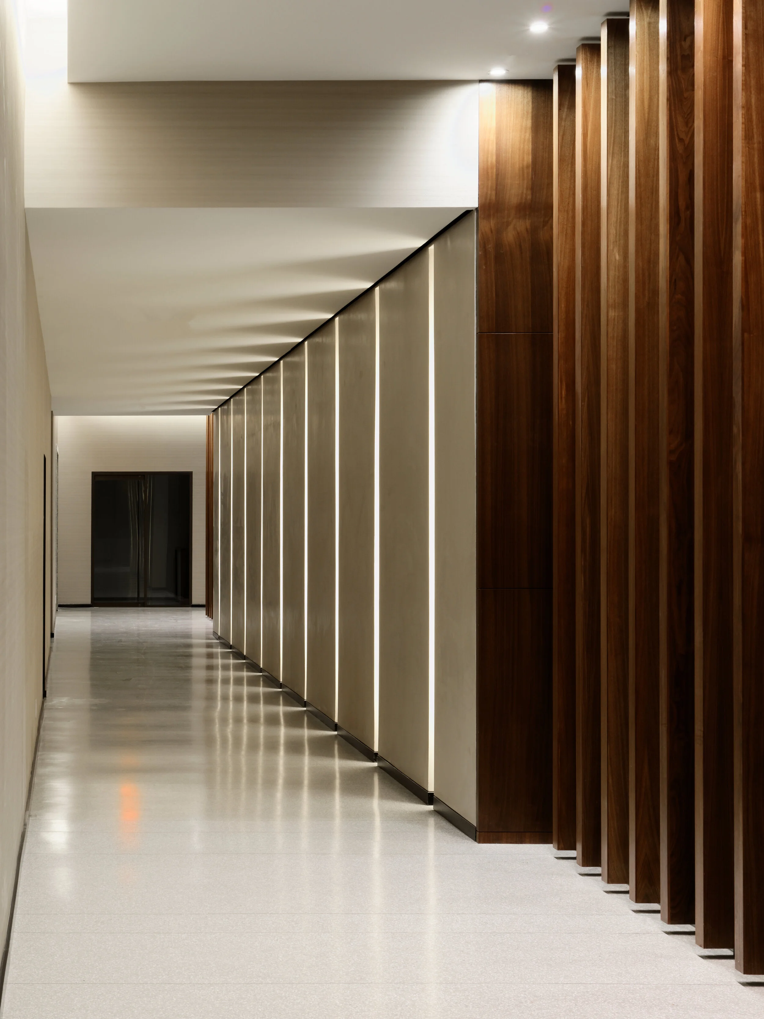 JGNA residential corridor lined with vertical walnut fins, backlit paneling, and polished stone flooring