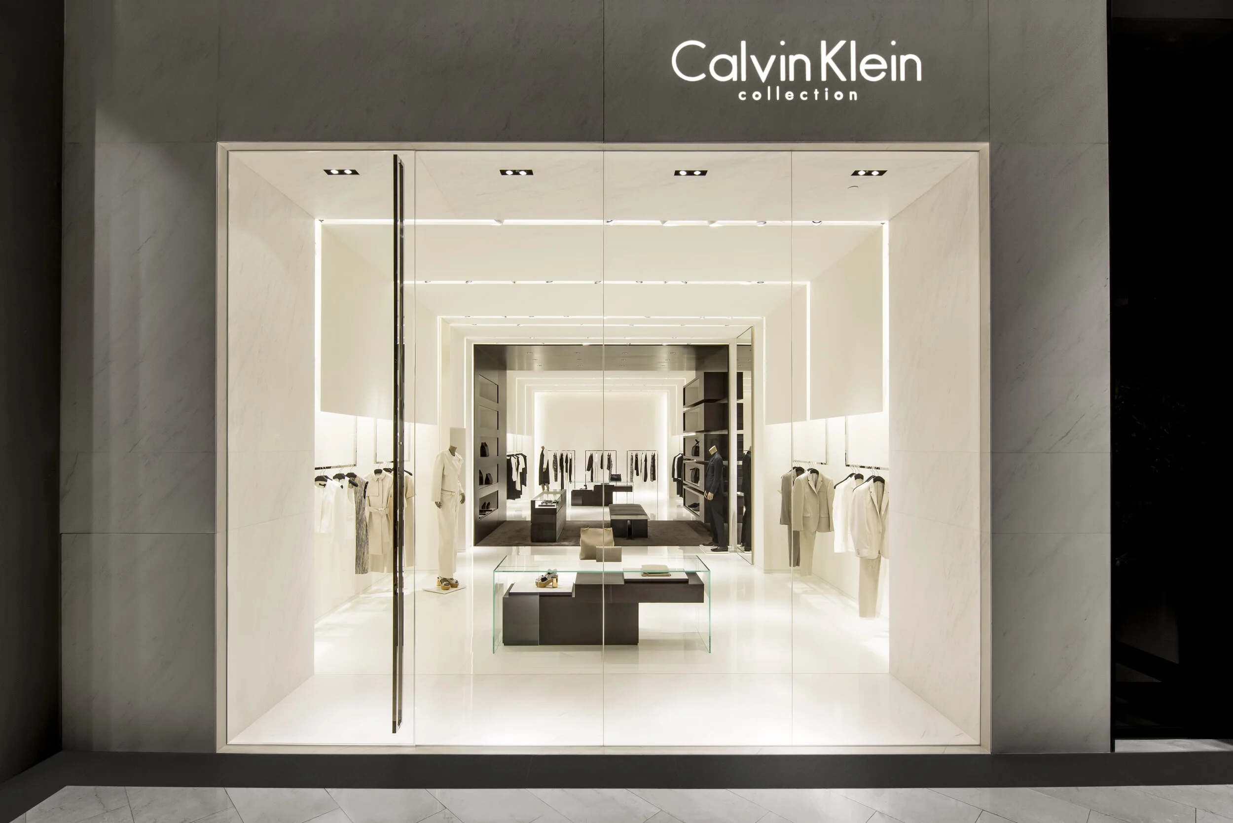 Calvin Klein Collection storefront with a marble surround, illuminated window display, and brand signage, designed by JGNA