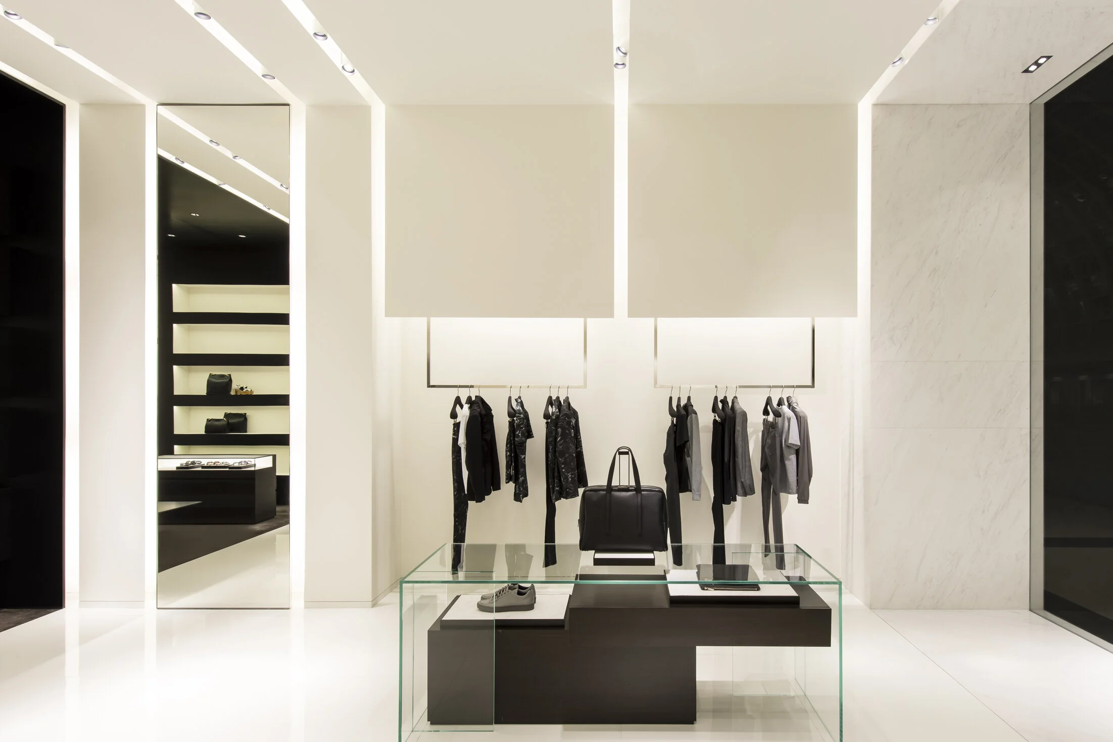 Calvin Klein Collection store interior with a full-length mirror, recessed shelving, marble wall, and glass display table
