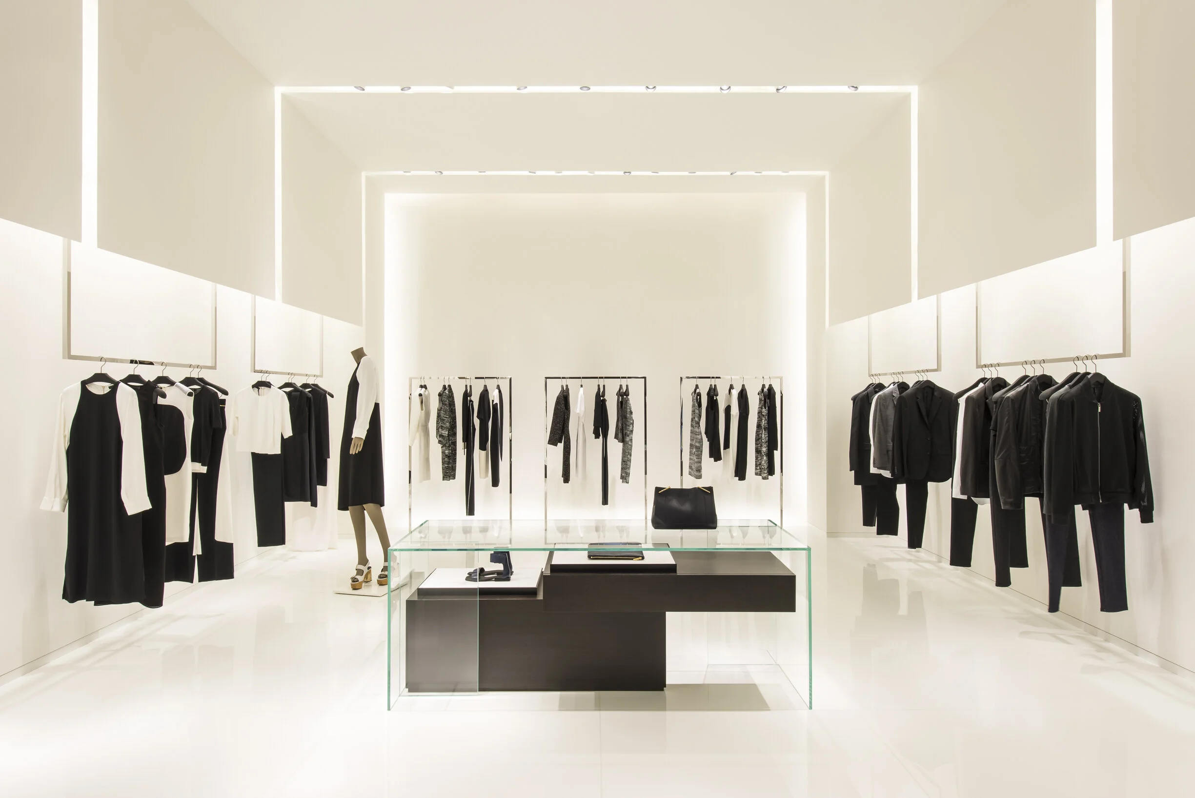 Calvin Klein Collection store with white womenswear rails, a central glass display table, and a mannequin, designed by JGNA