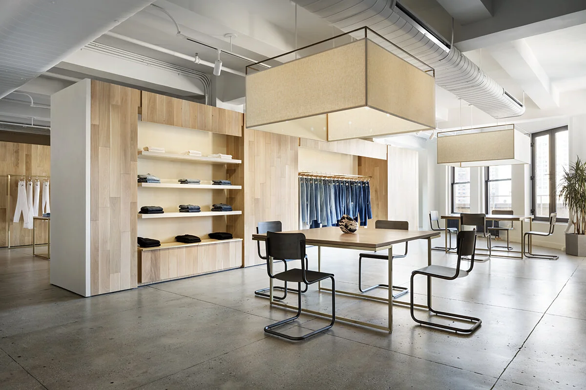 JGNA-designed FRAME Denim showroom with oak paneling, fabric box pendants, a wood table, and cantilever chairs