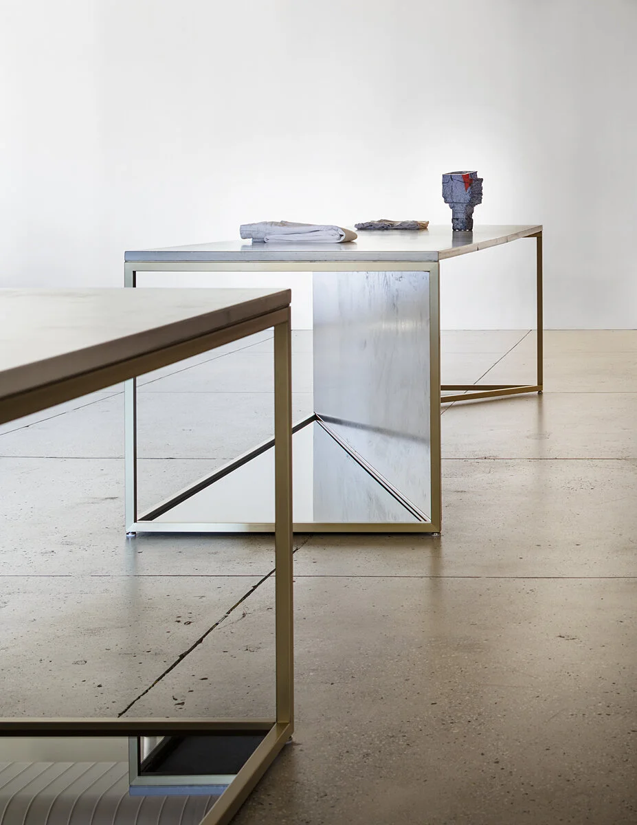 FRAME Denim showroom detail of a brass-framed mirrored display table on polished concrete flooring