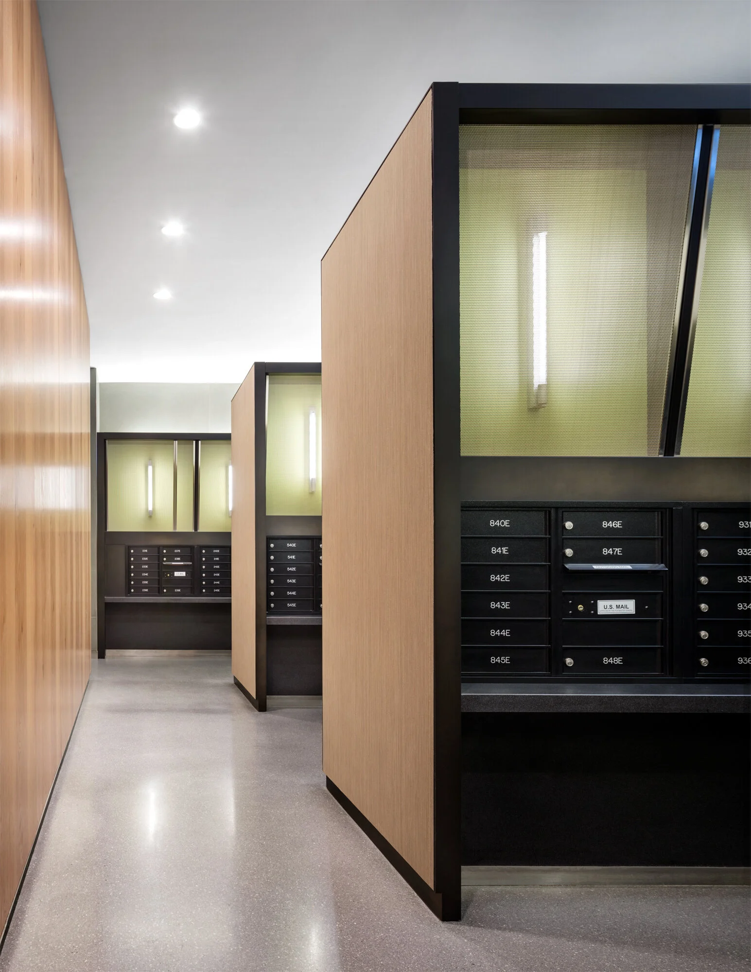 JGNA residential mailroom with oak-clad mailbox stations, green-backed niches, and a terrazzo floor