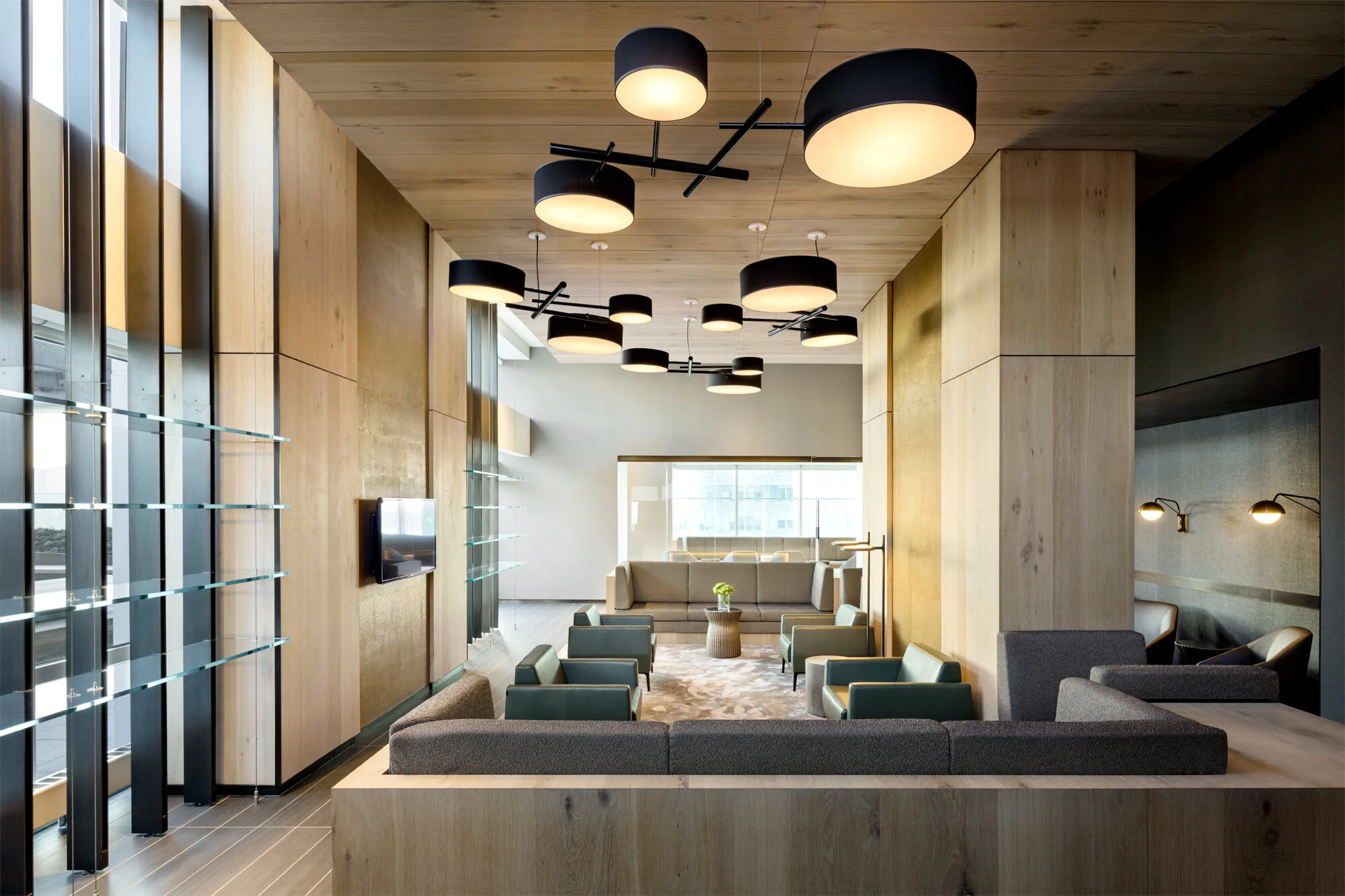 JGNA residential lounge with sunken seating, black drum pendants, oak walls, and a glass shelf window wall