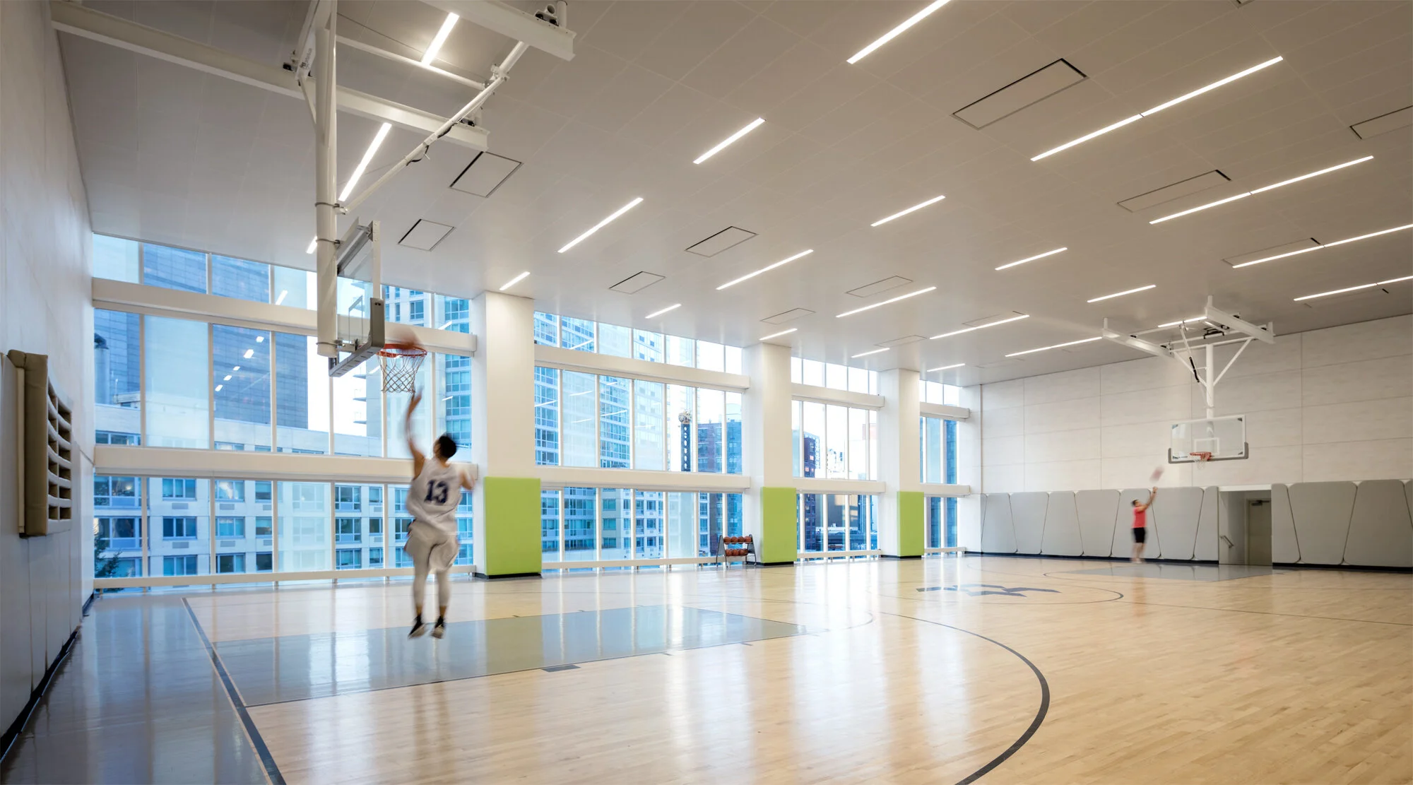 JGNA residential indoor basketball court with a glossy floor, full-height windows, and a player mid-jump
