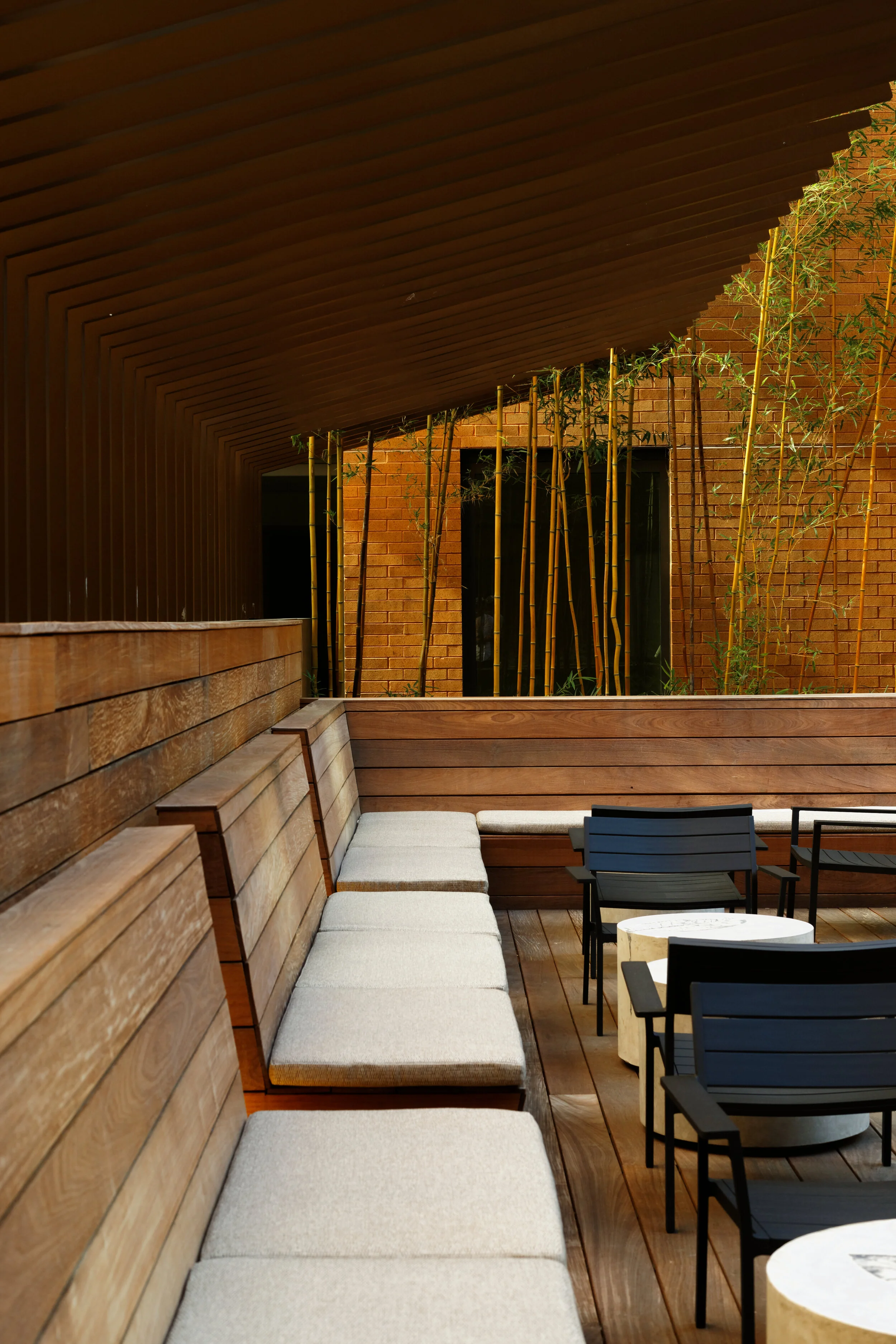 JGNA residential sunken lounge with a timber banquette, slat ceiling, and bamboo-planted courtyard