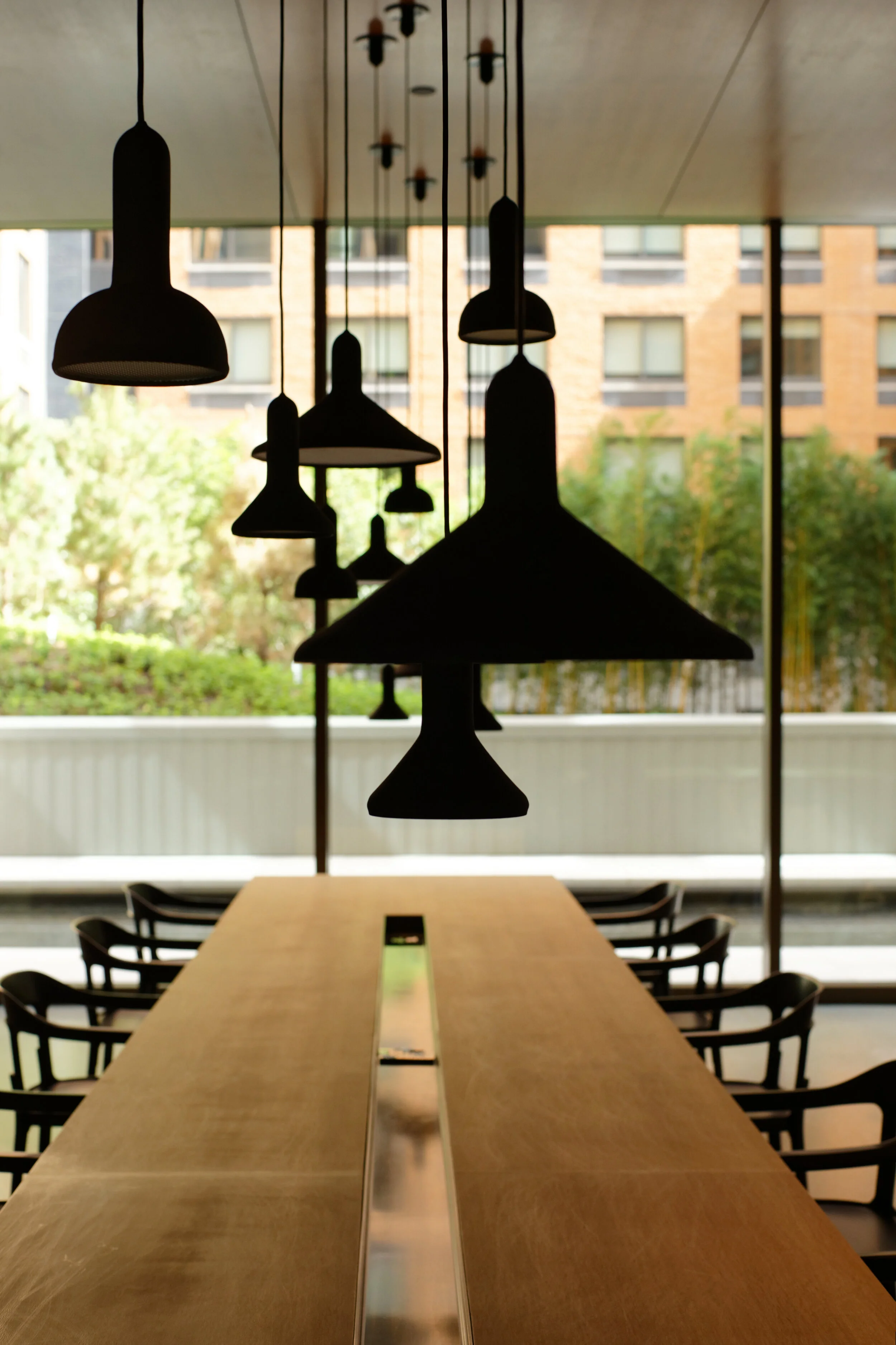 JGNA residential communal oak table with a row of black pendants overlooking a planted terrace