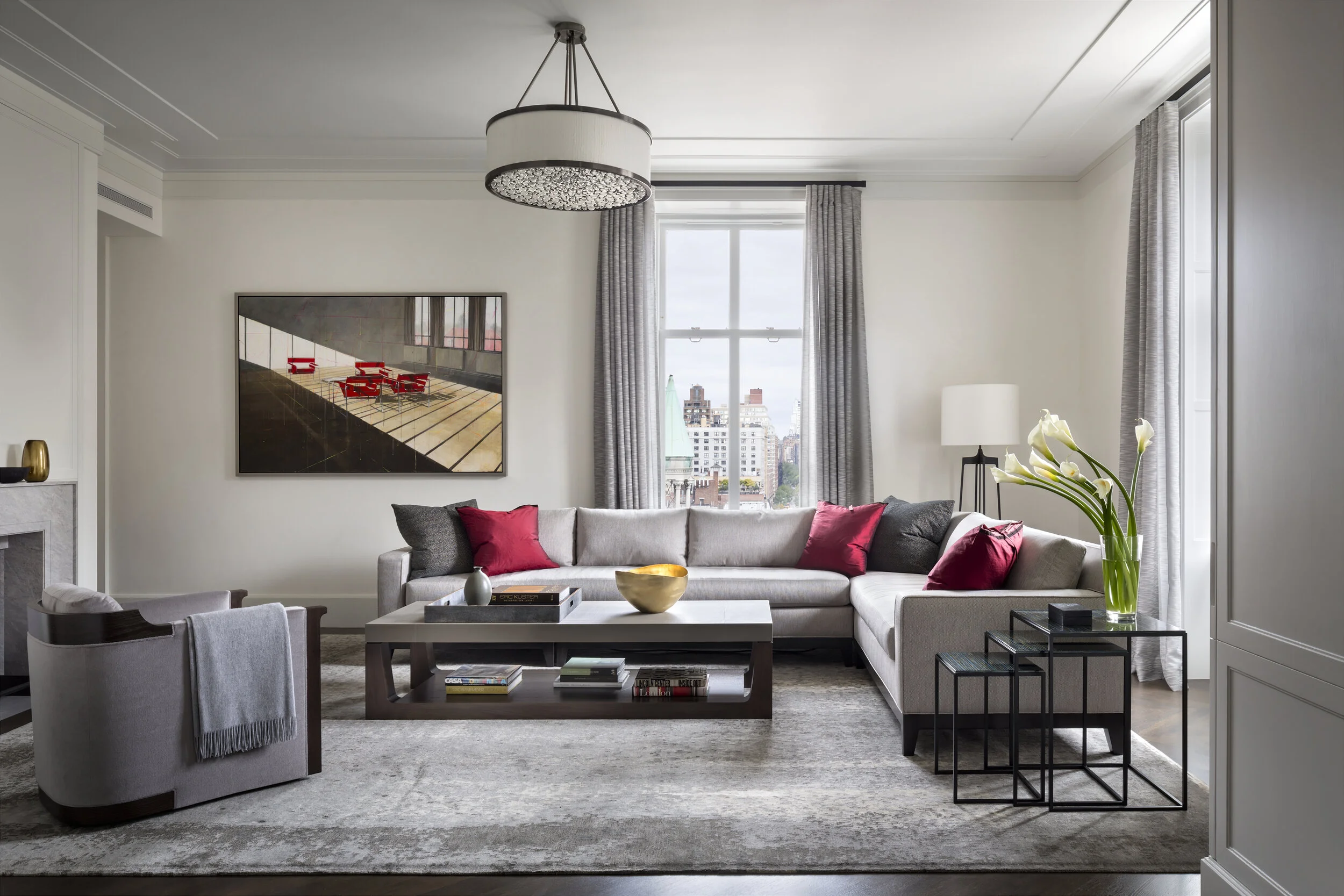 JGNA residence living room with a grey sectional, marble fireplace, drum chandelier, and a city view