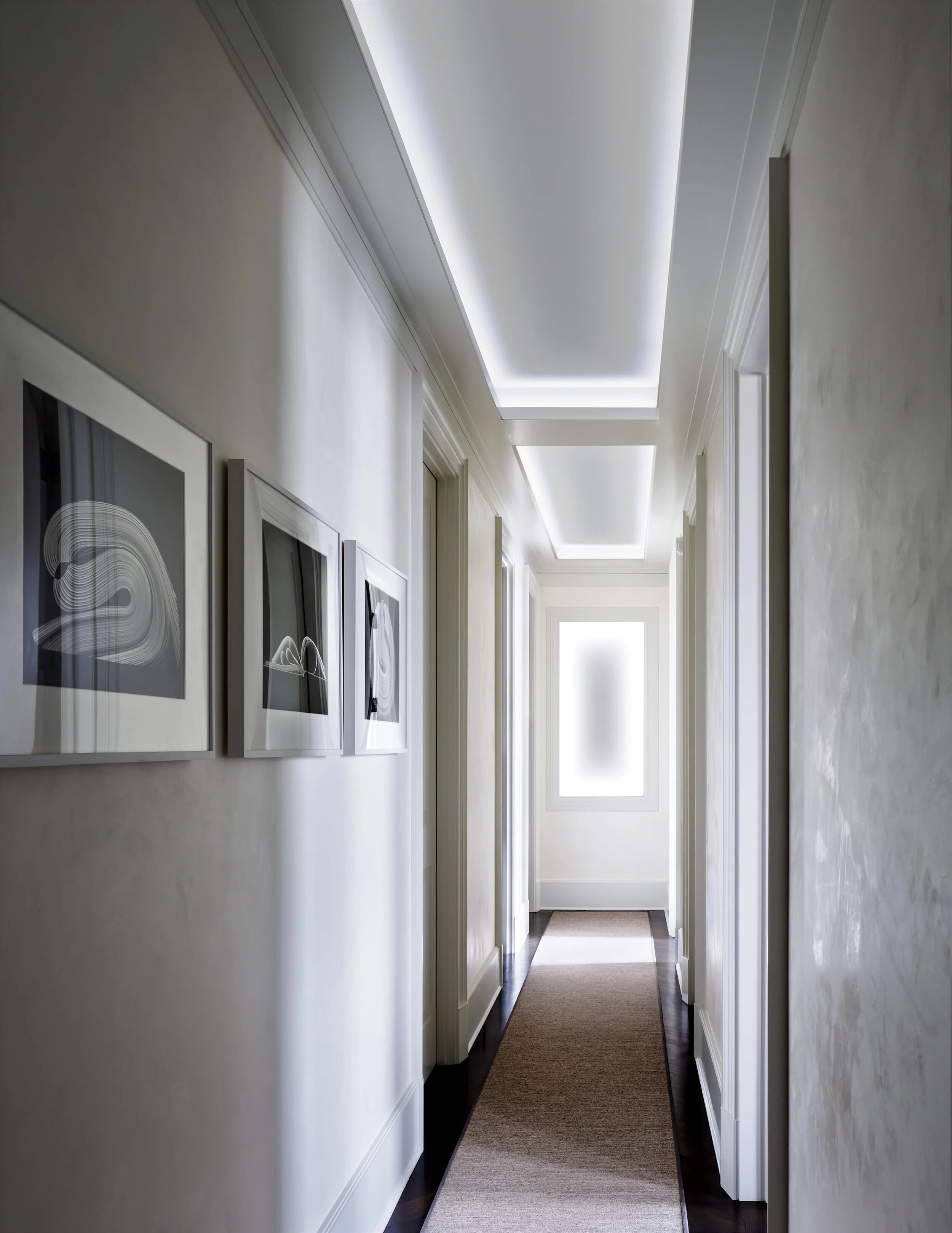 JGNA residence gallery hallway with framed black-and-white photographs and a backlit cove ceiling