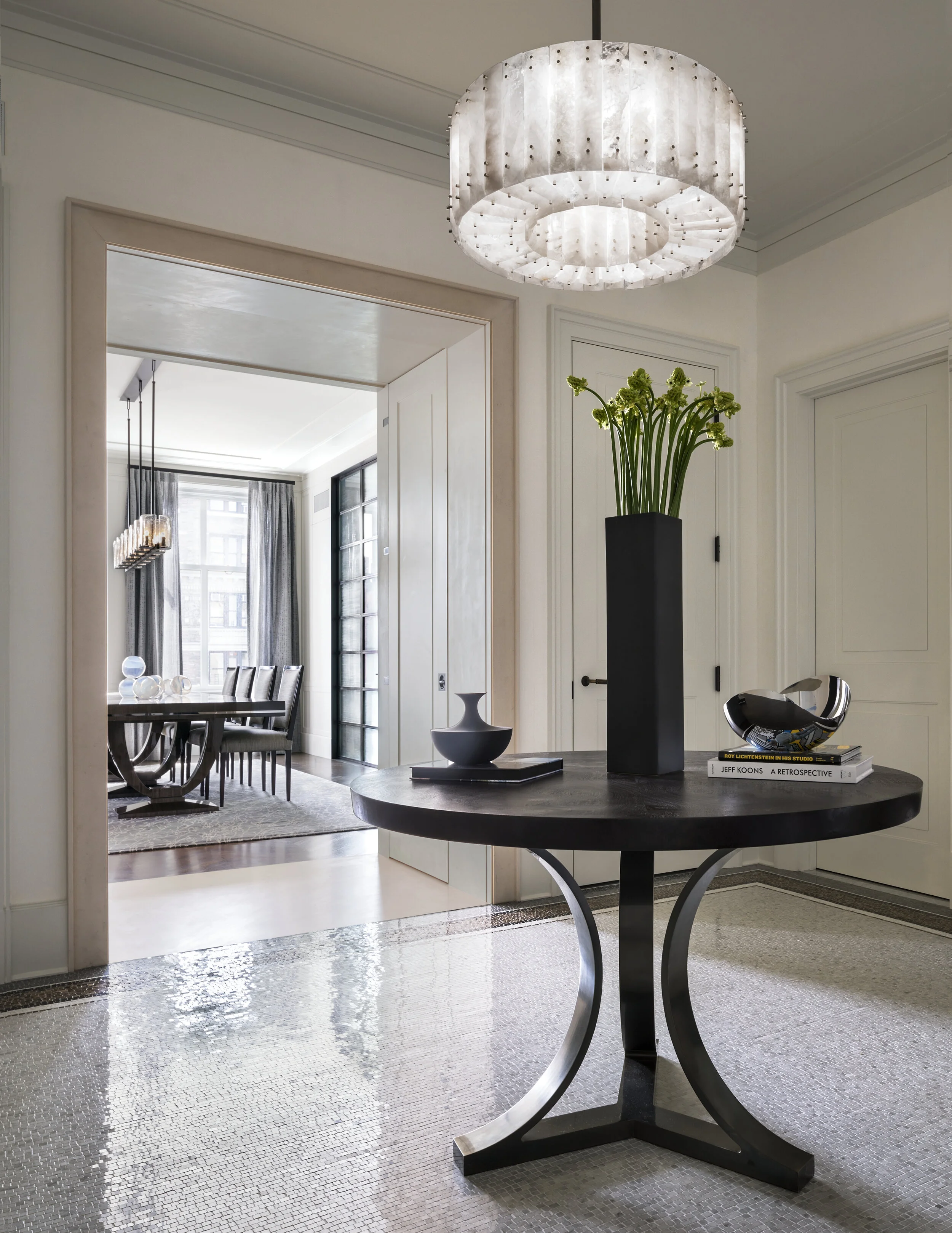 JGNA residence entry foyer with a round pedestal table, mosaic floor, and a tiered shell pendant