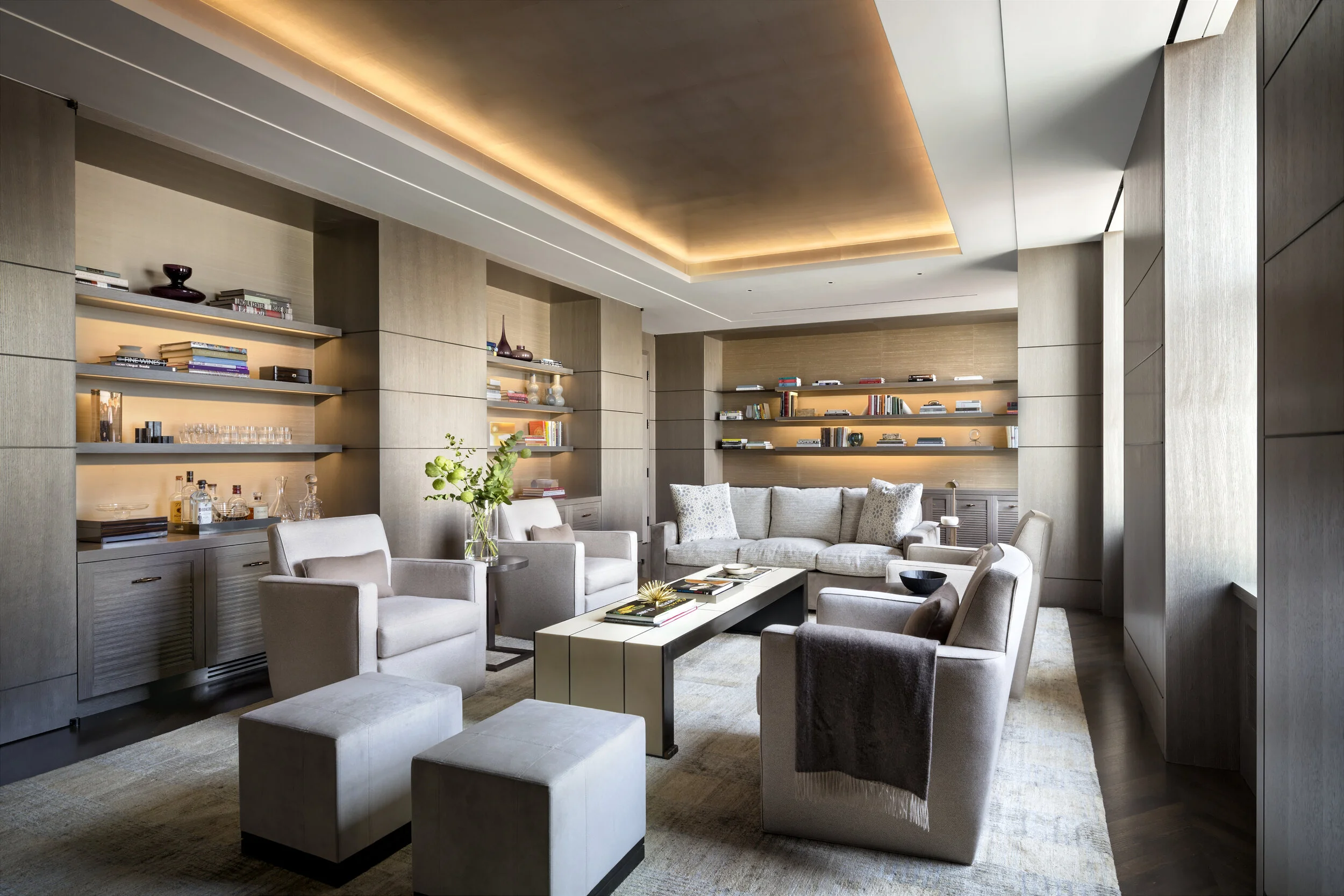 JGNA residence living room with backlit oak shelving, a recessed cove-lit ceiling, and neutral upholstered seating