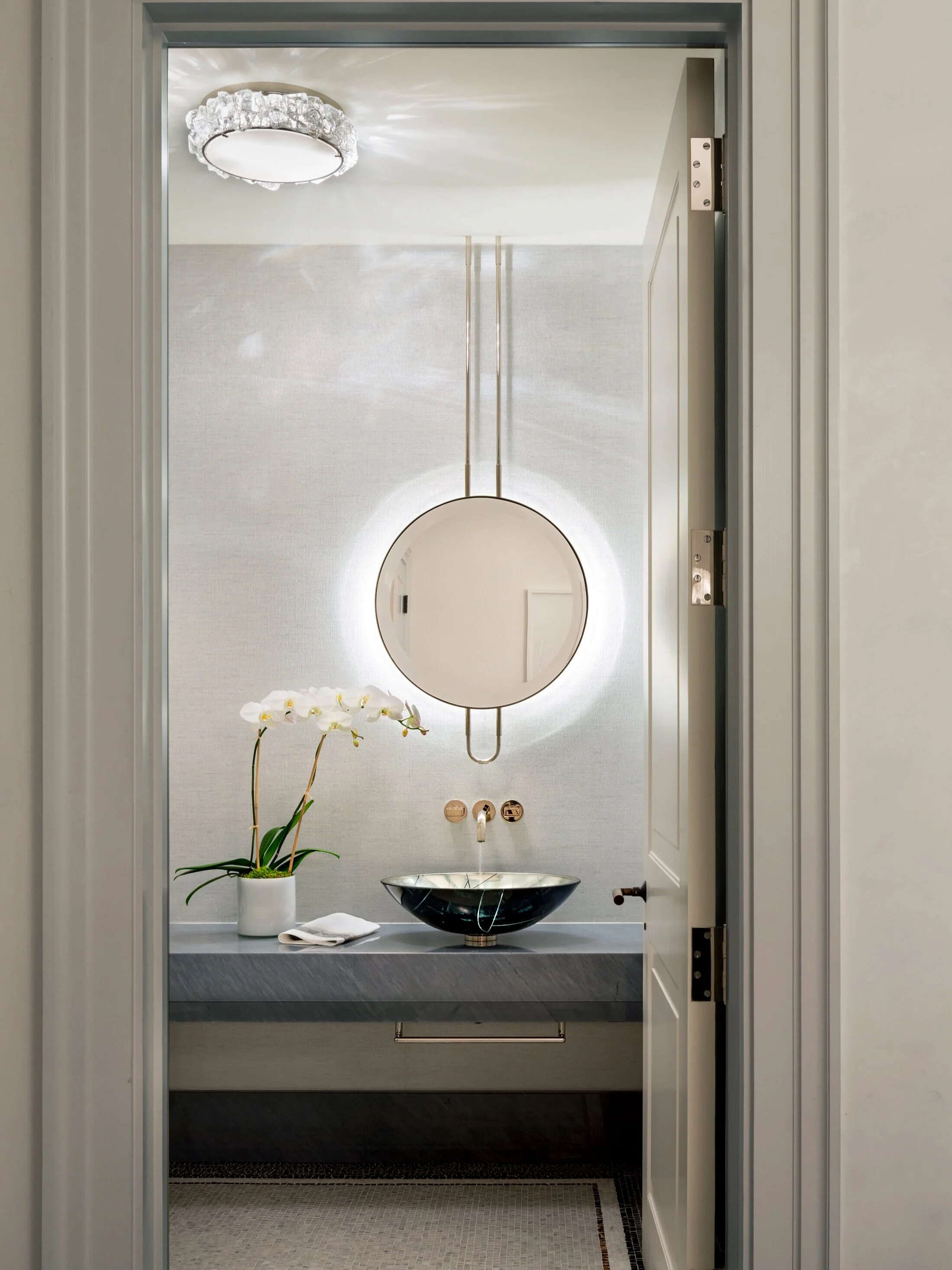 JGNA residence powder room with a backlit round mirror, floating vanity, and a stone vessel sink
