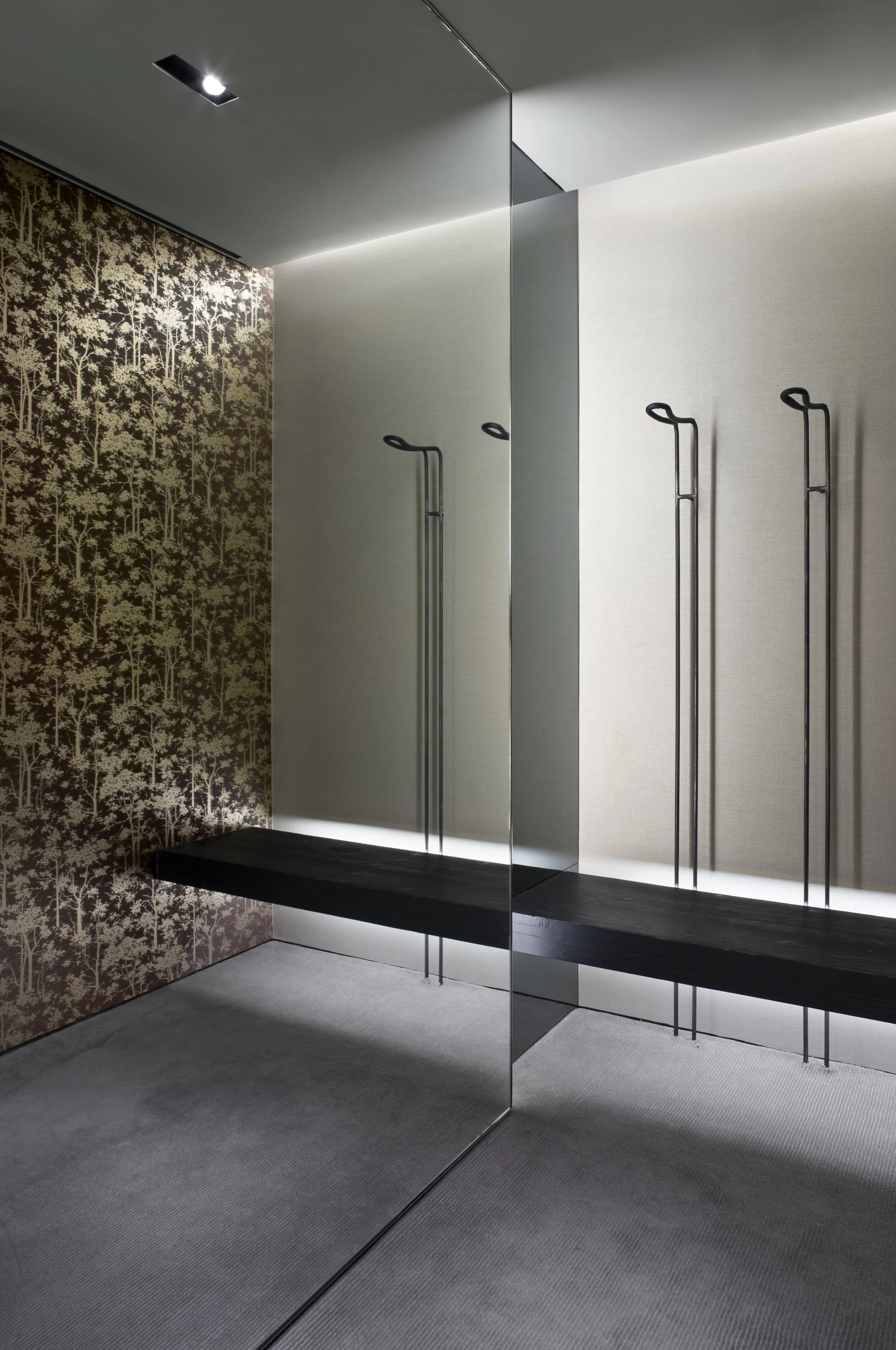 JGNA fitting room with mirrored walls, a floating black bench, slim metal hooks, and a patterned gold wall