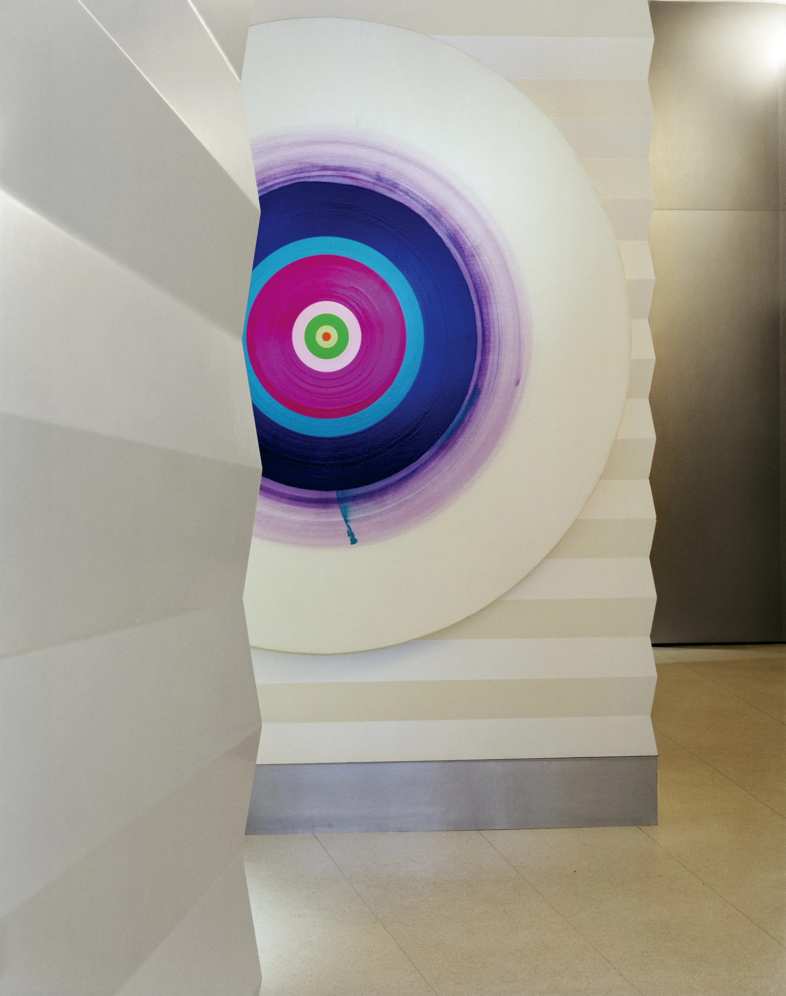 JGNA lobby with a sculptural curved wall, a large concentric-circle painting, and polished stone flooring