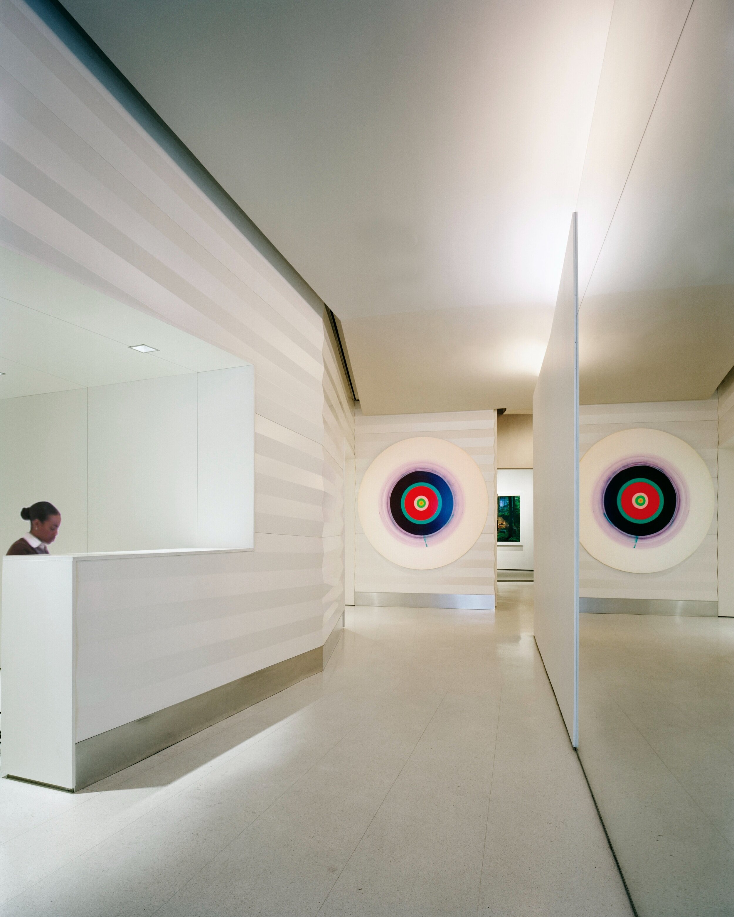 JGNA lobby reception desk with target-motif paintings along rippled white walls and a receptionist