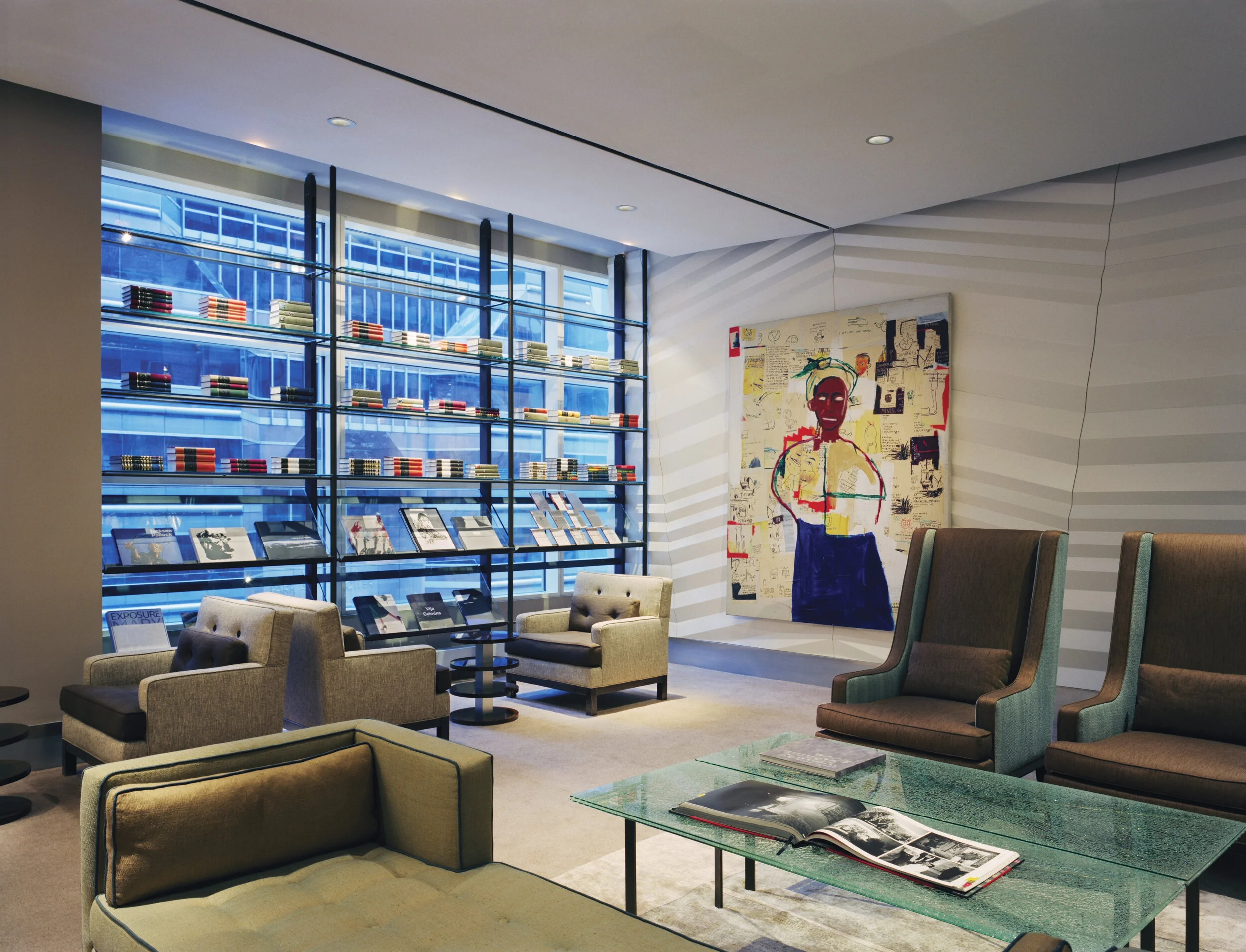 JGNA lounge with a glass-and-steel bookshelf wall, large figurative painting, and upholstered armchairs