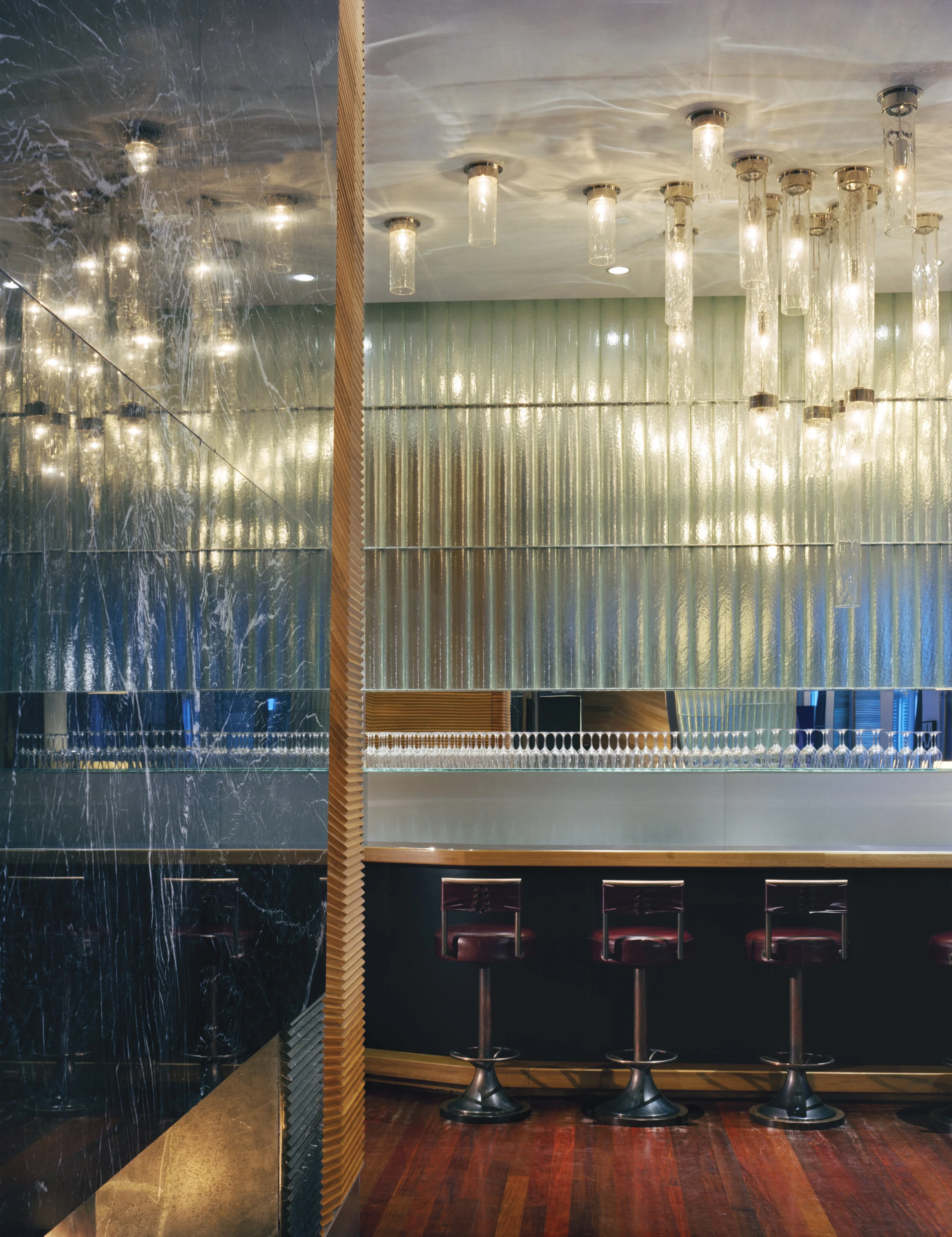 JGNA bar with a backlit glass-rod ceiling canopy, red leather stools, and a dark marble wall
