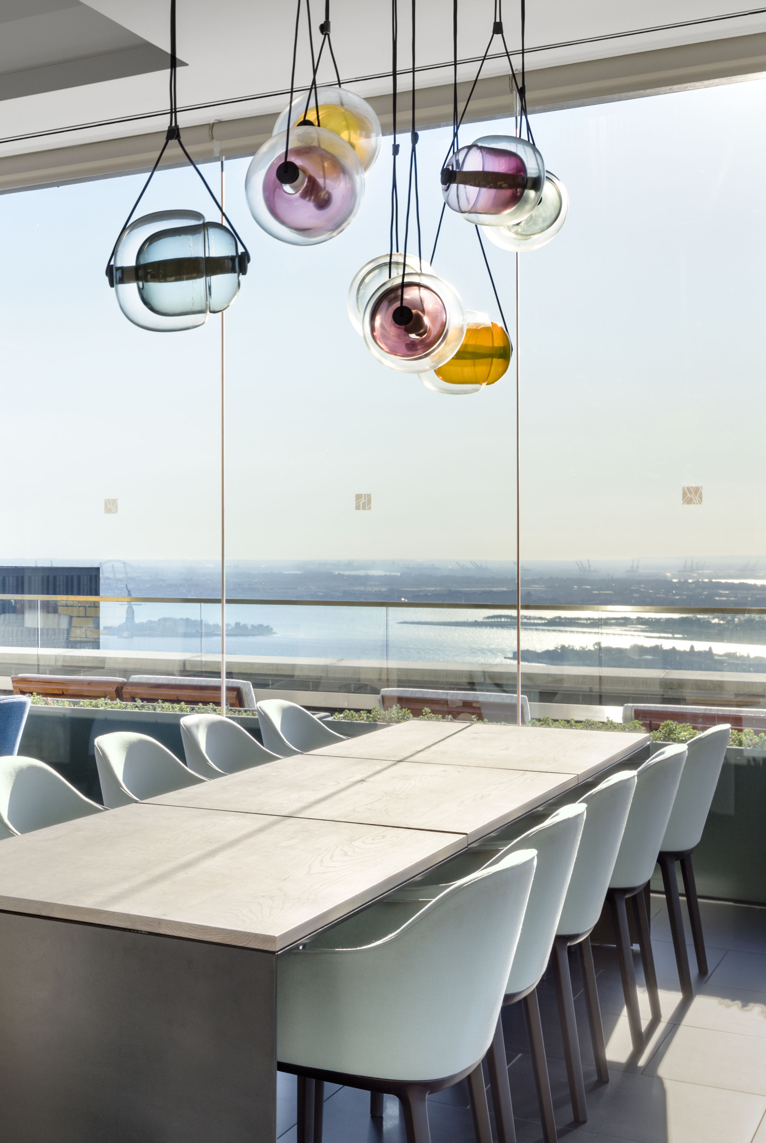 JGNA penthouse dining room with a cluster of colored glass pendant lights and a stone table by the window