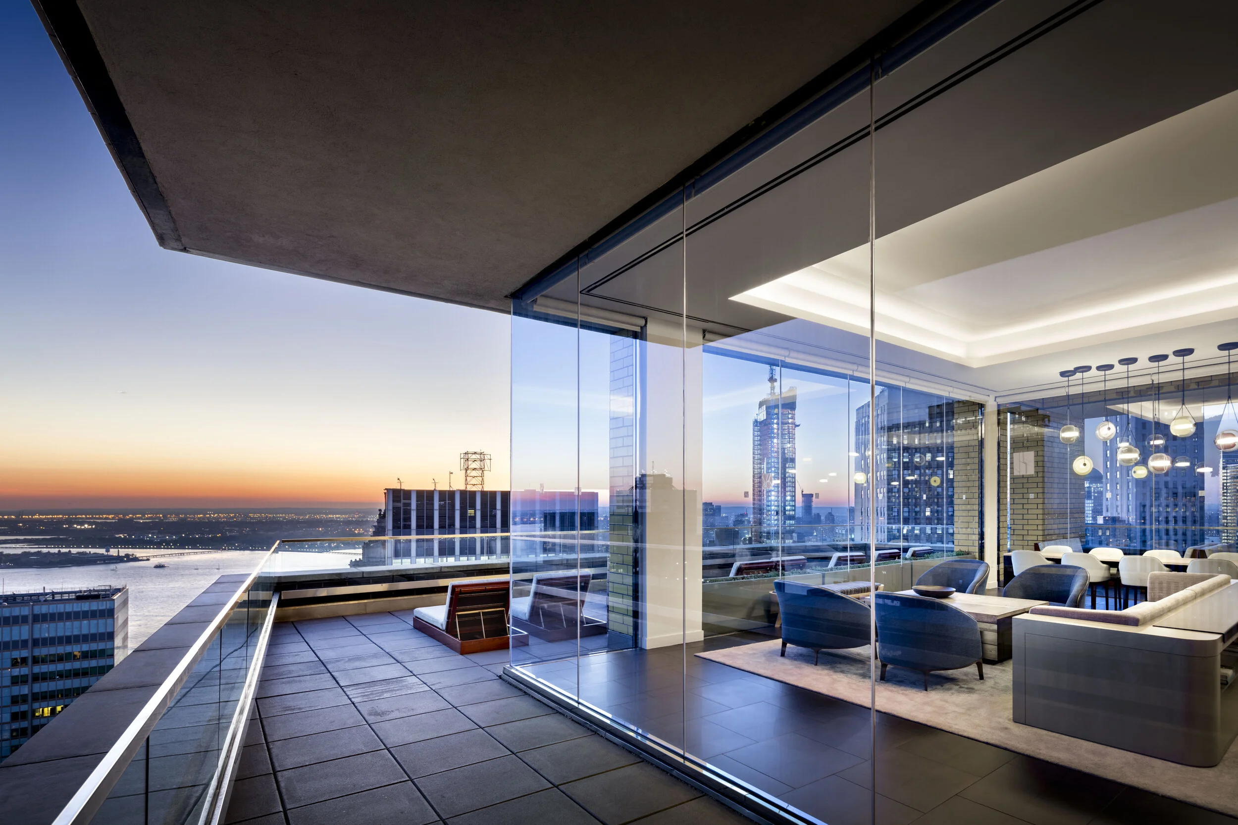 JGNA penthouse living room with floor-to-ceiling glass, a wraparound terrace, and a sunset city skyline view
