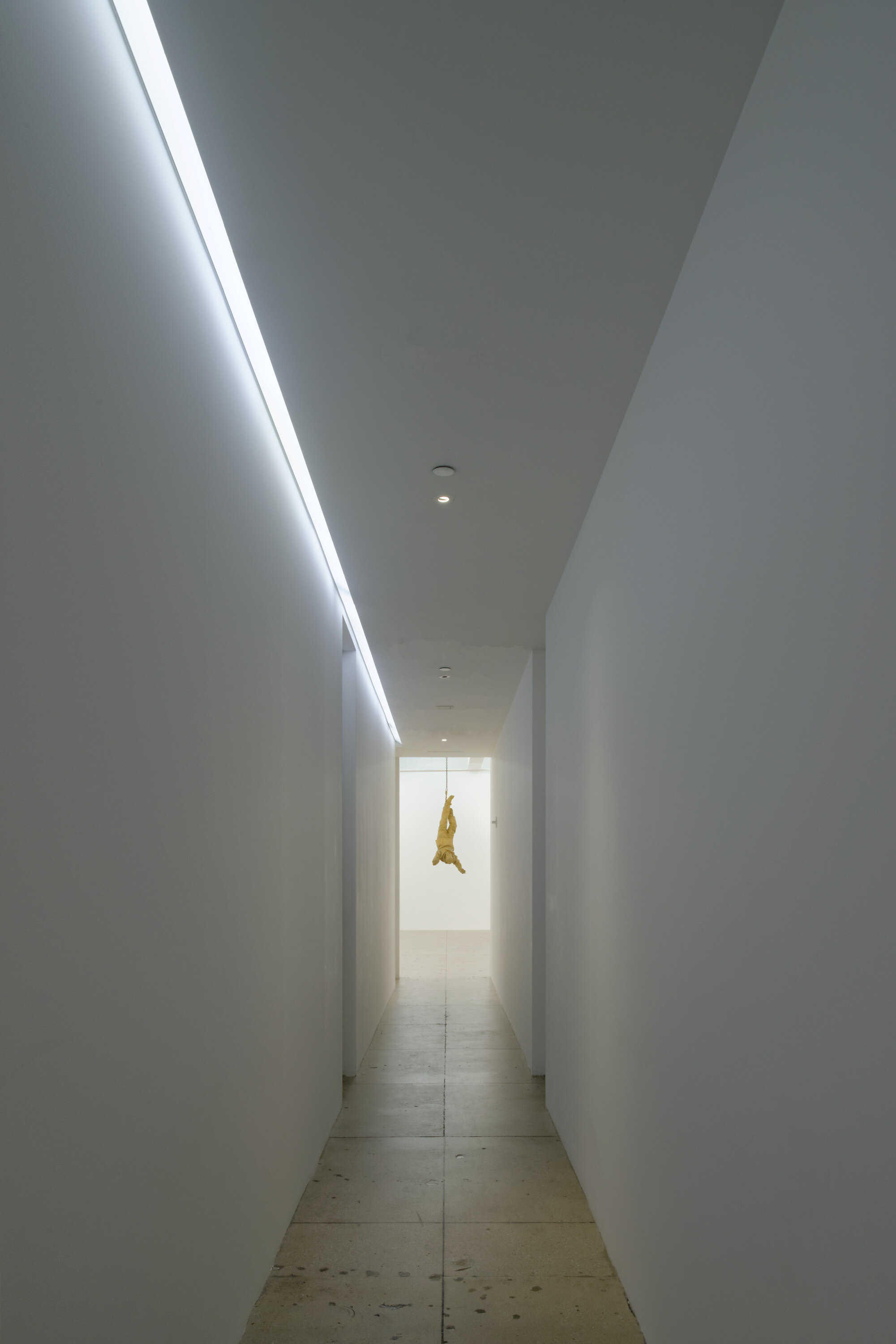 Marian Goodman Gallery corridor with recessed cove lighting and a suspended golden figurative sculpture at the far end