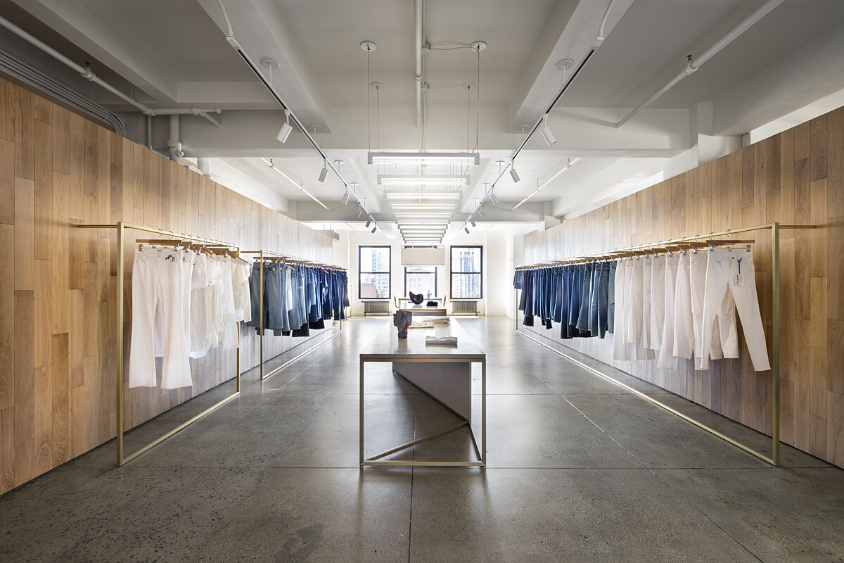 FRAME Denim showroom with symmetrical garment rails on oak walls and a central brass display table, designed by JGNA