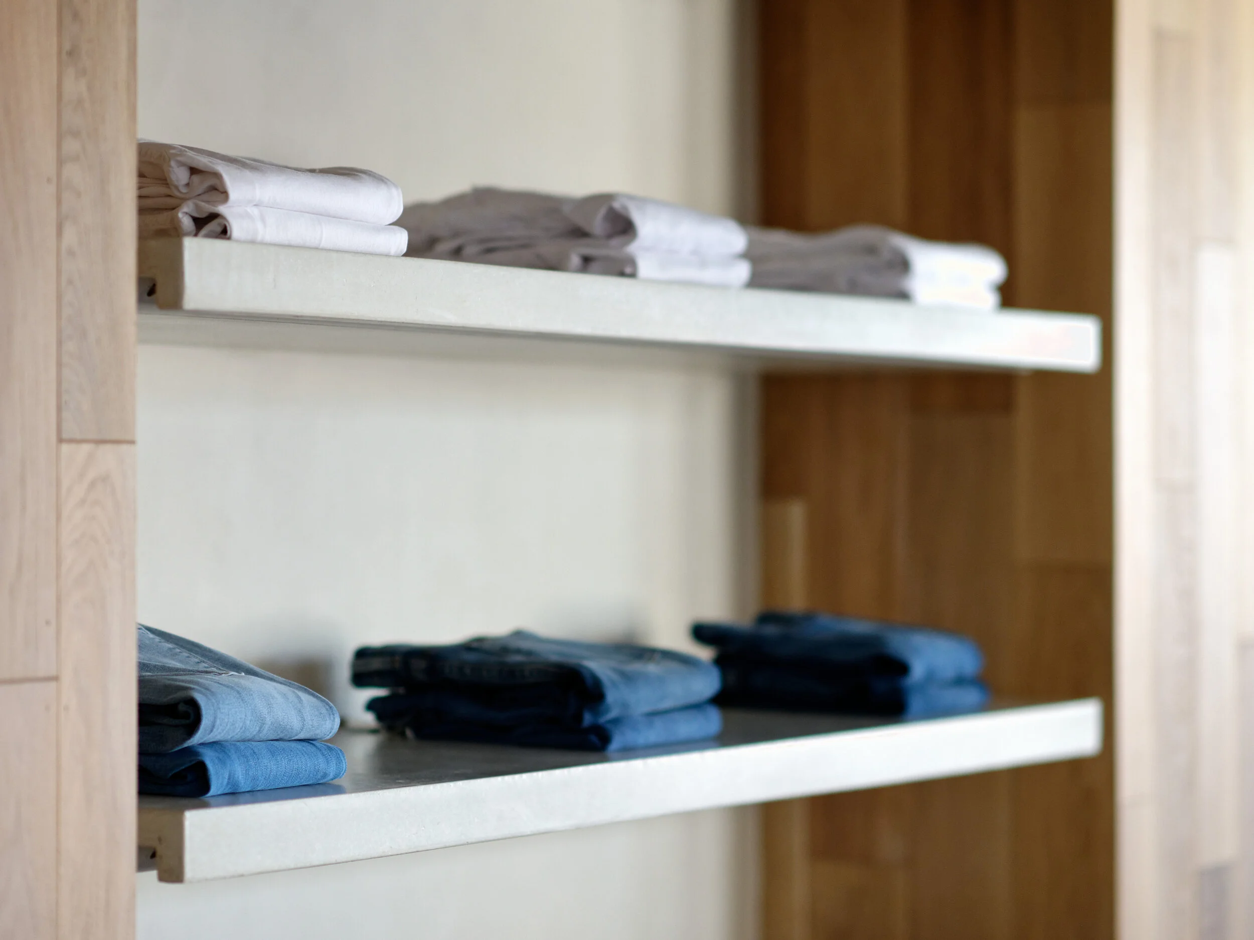 FRAME Denim showroom detail of white floating shelves with folded jeans and tees against oak paneling