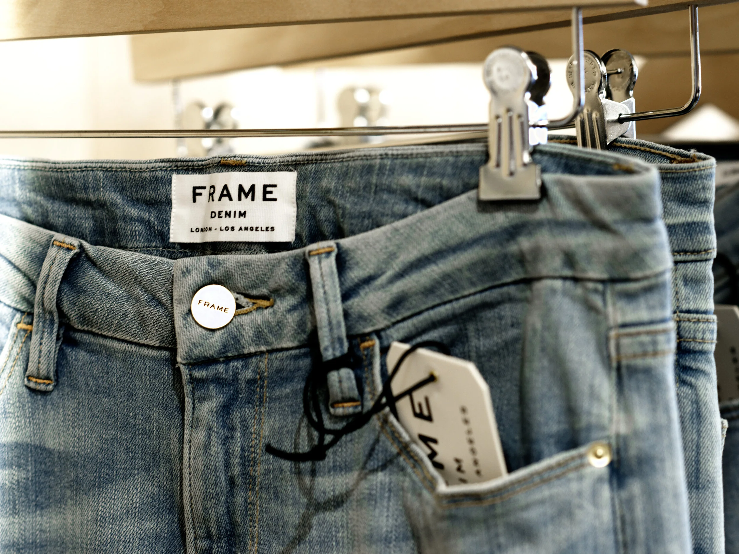 FRAME Denim jeans on a hanger showing the brand label and tag in the showroom