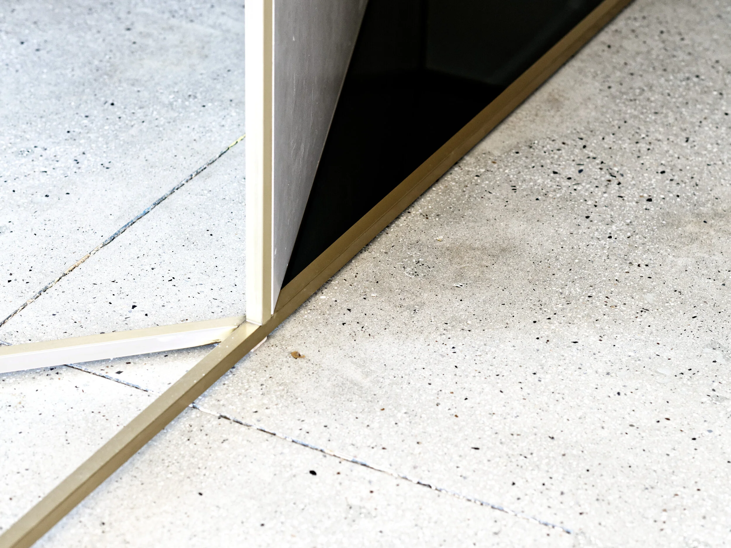 FRAME Denim showroom close-up of a brass mirror edge meeting polished concrete flooring