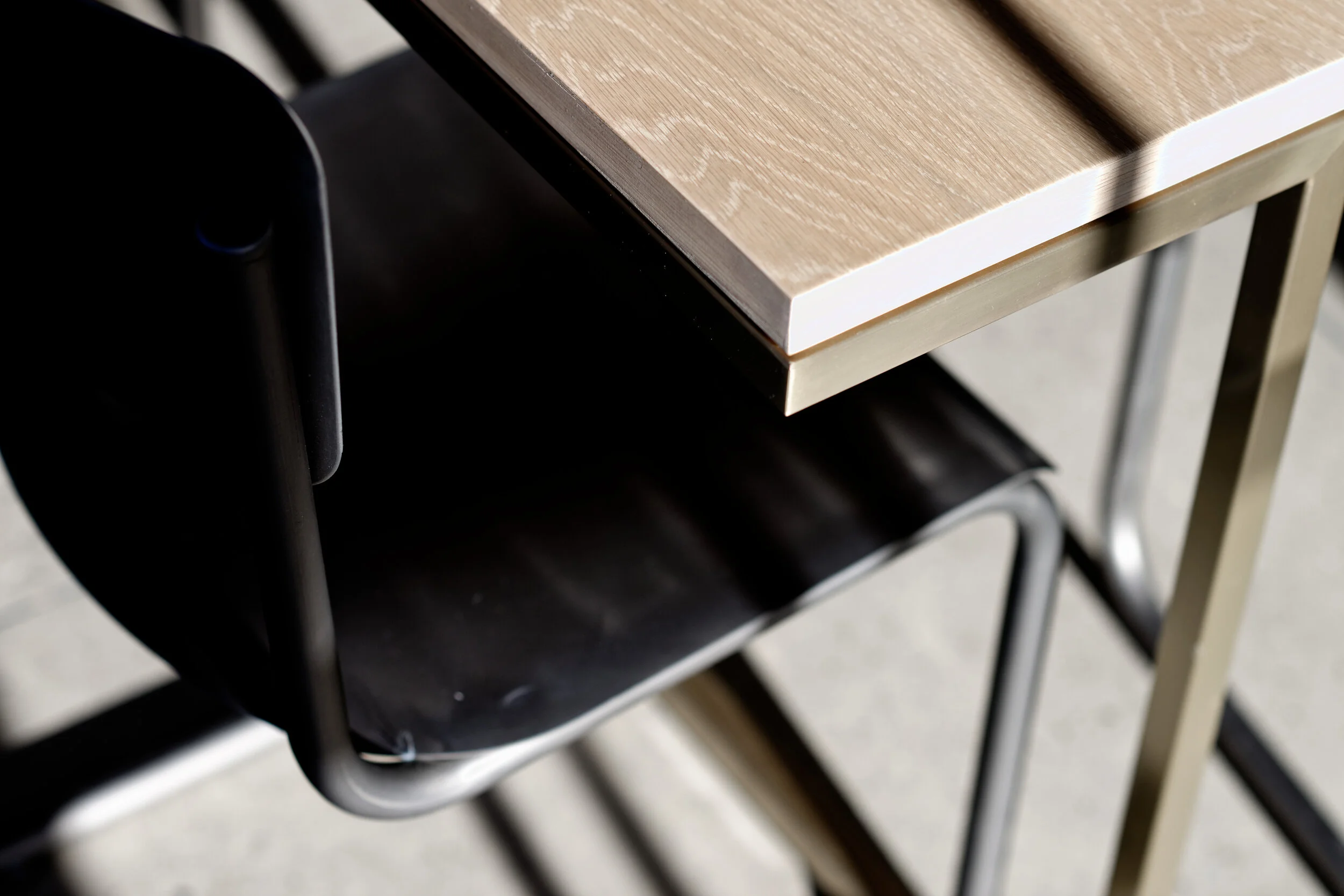 FRAME Denim showroom detail of an oak table edge with a brass frame and black cantilever chair