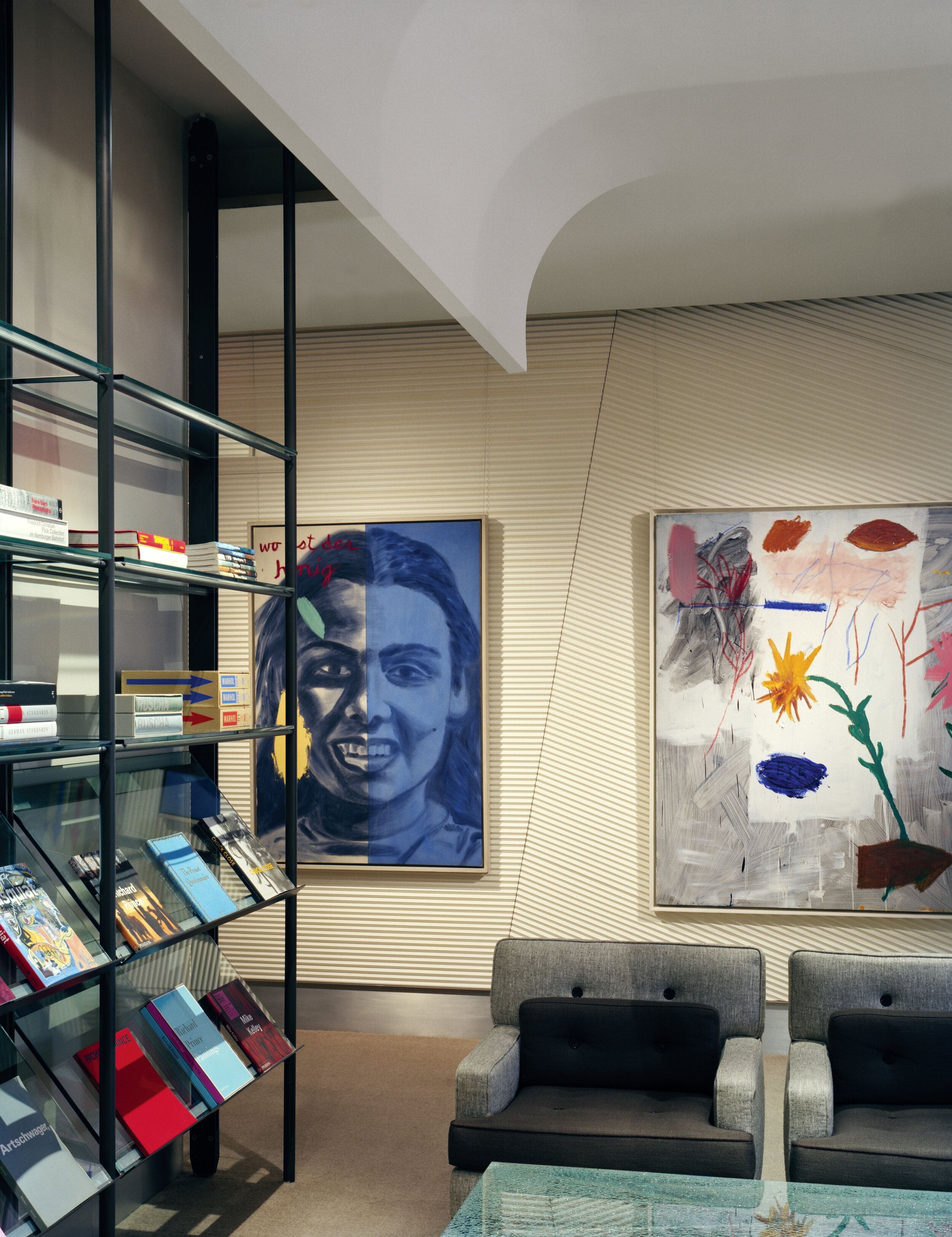 JGNA lounge with steel magazine shelving, a blue portrait painting, and a large abstract canvas