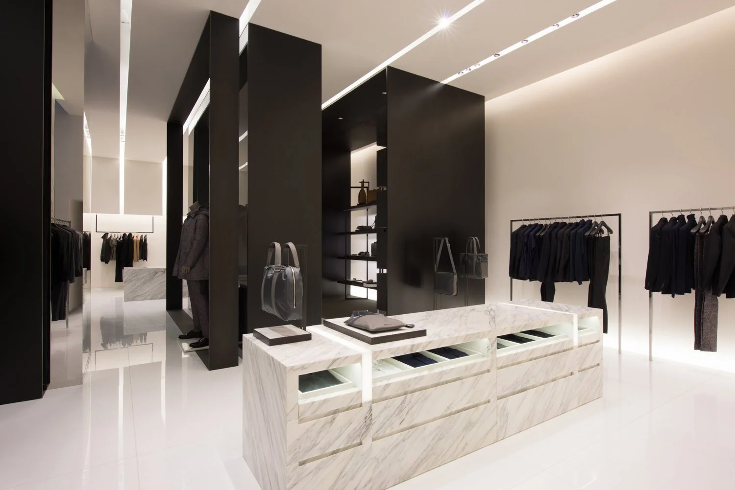 Calvin Klein Collection store with a marble island counter, black display volumes, and menswear rails, designed by JGNA