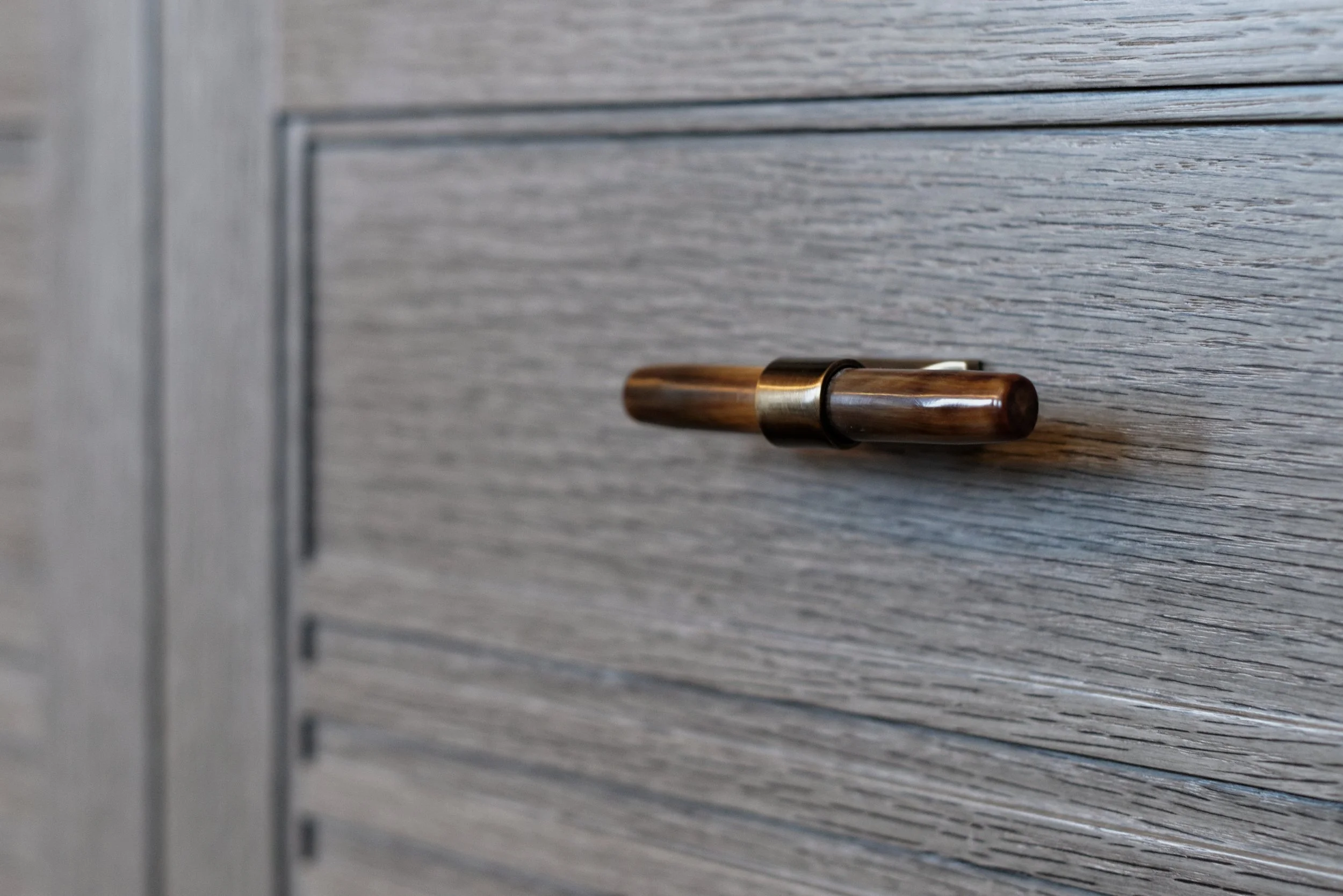 JGNA residence detail of a bronze and leather drawer pull on a cerused oak cabinet