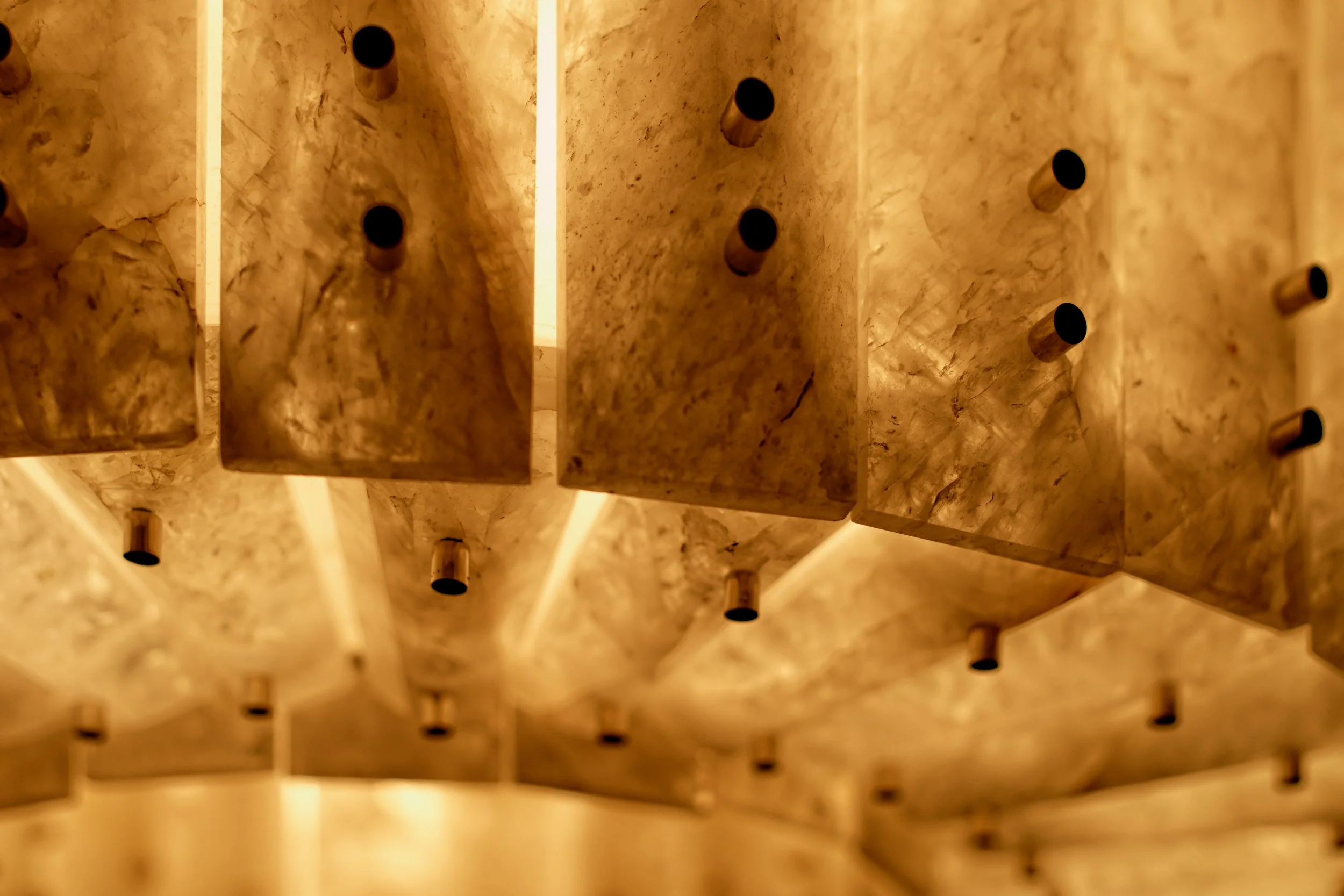 JGNA residence detail of a backlit onyx stone wall with projecting bronze pegs