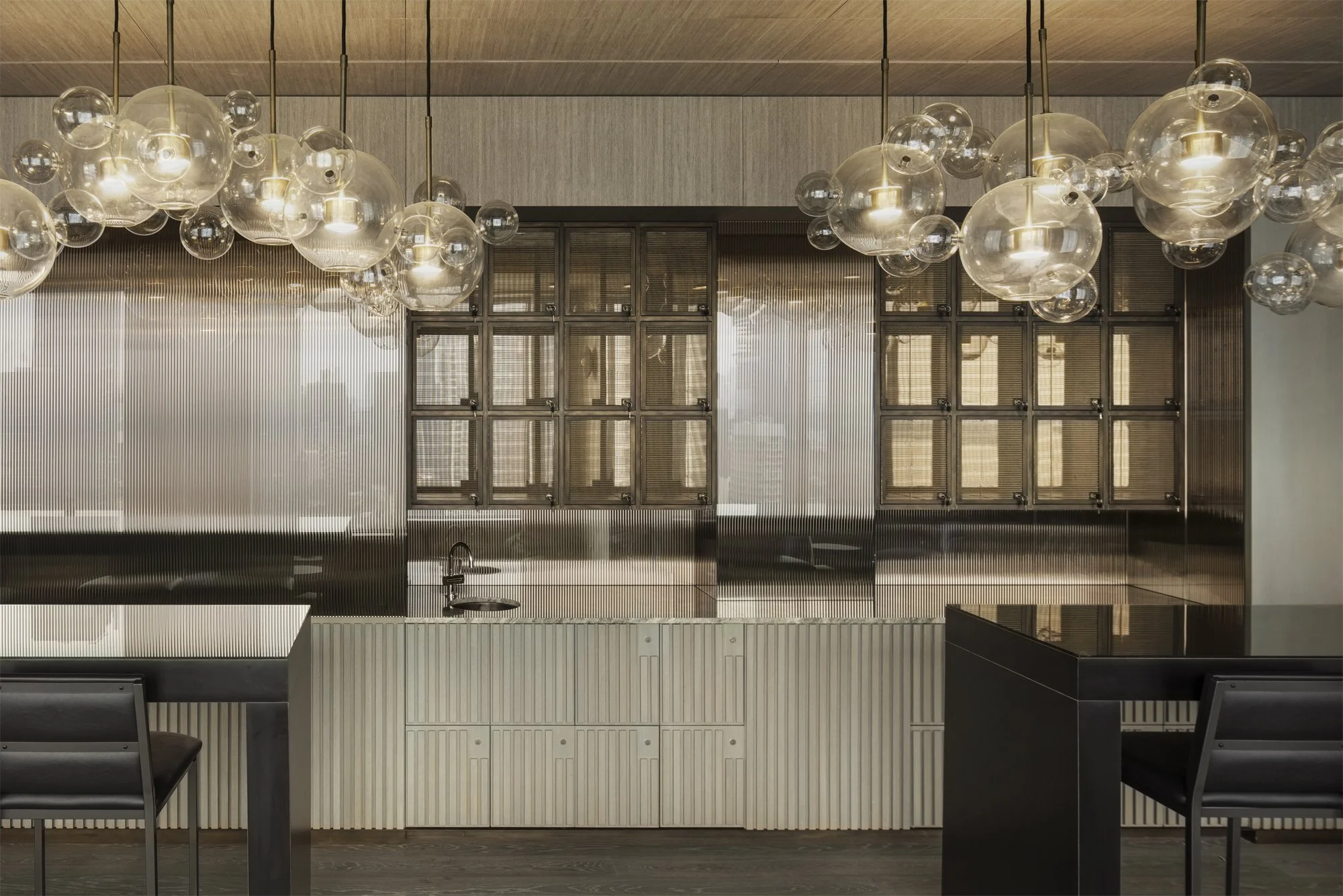 JGNA residential entertaining kitchen with a bubble glass chandelier, fluted glass cabinetry, and a dark island