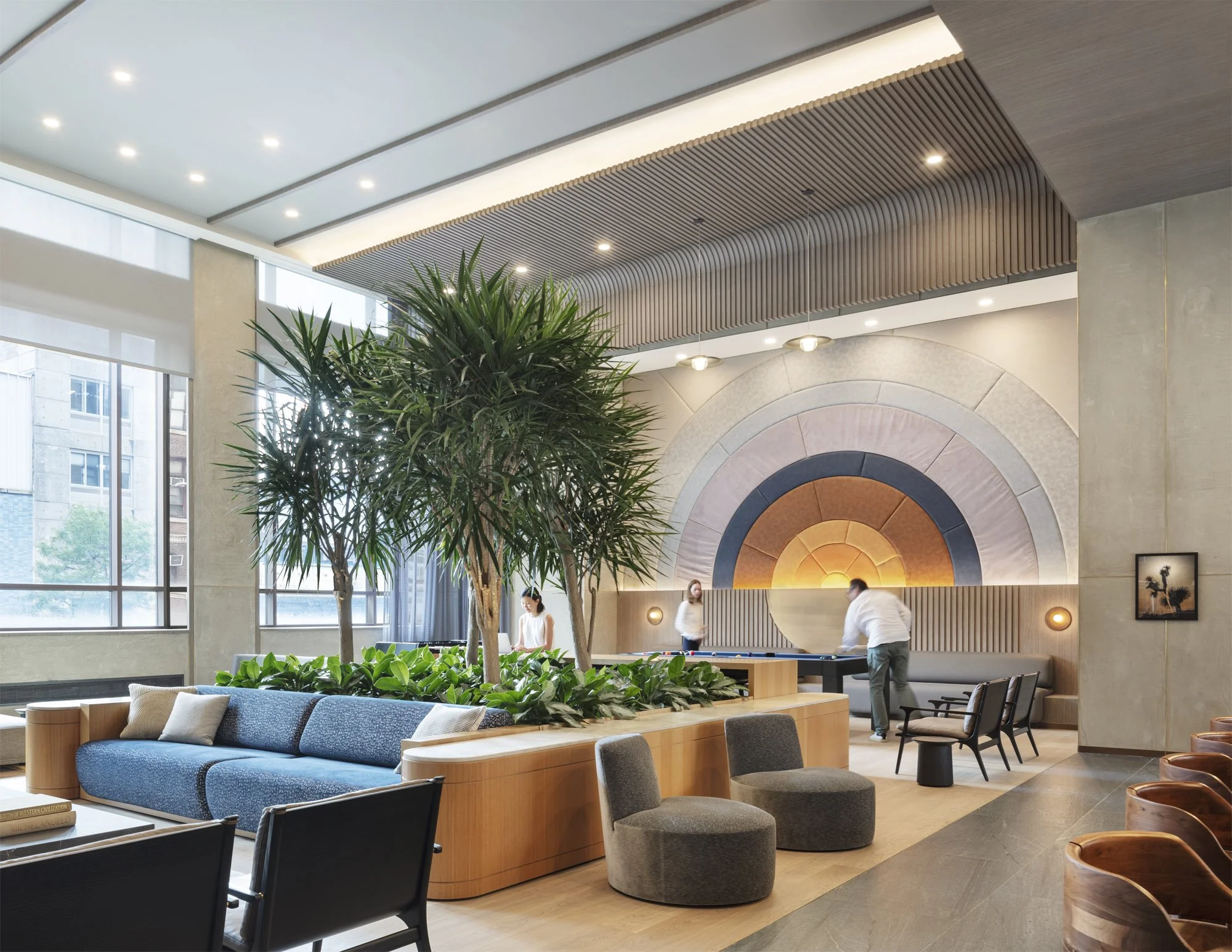 JGNA residential lounge with an arched backlit feature wall, blue sofa, built-in planters, and interior trees