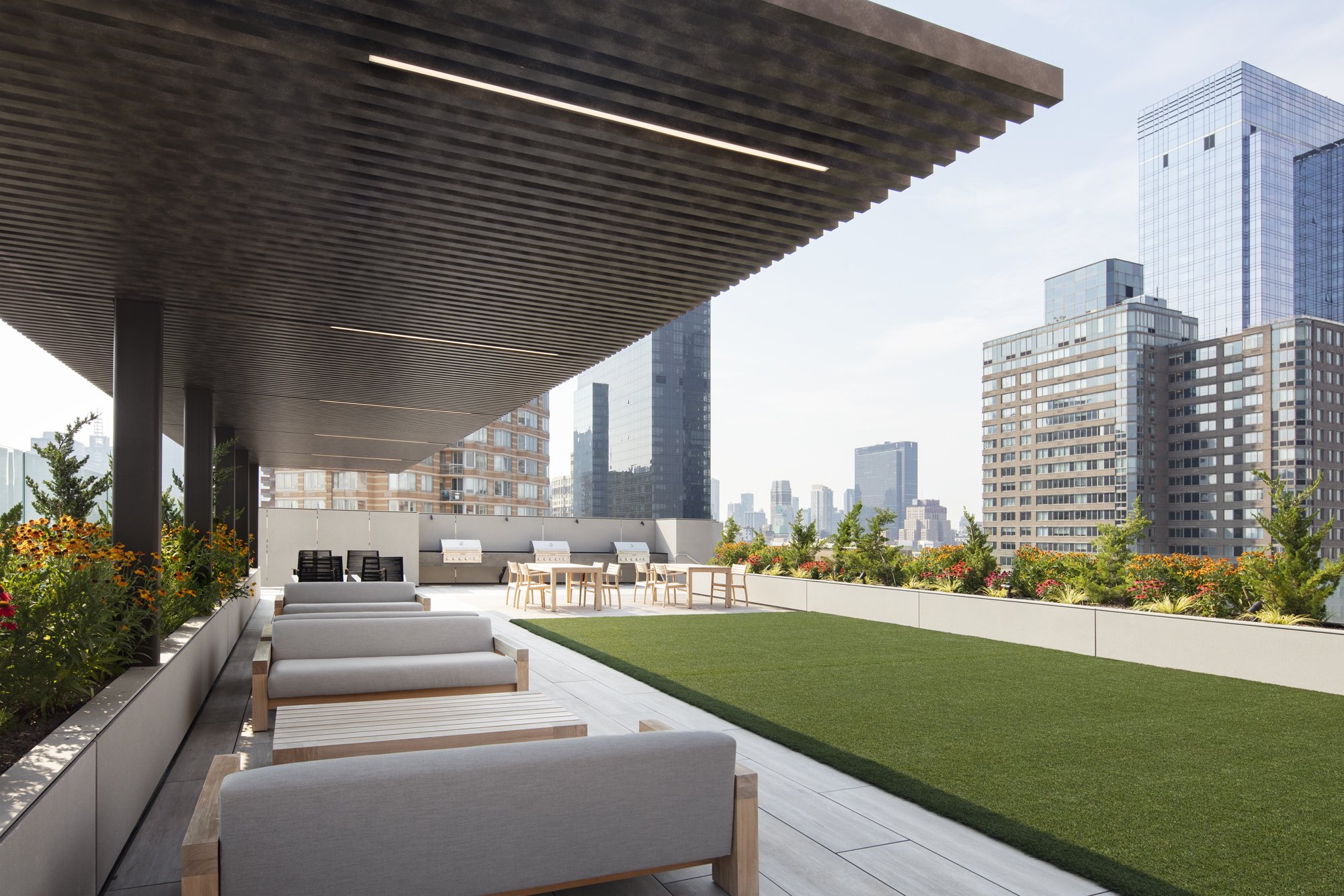 JGNA residential rooftop terrace with cushioned loungers under a slatted canopy and a Manhattan skyline view