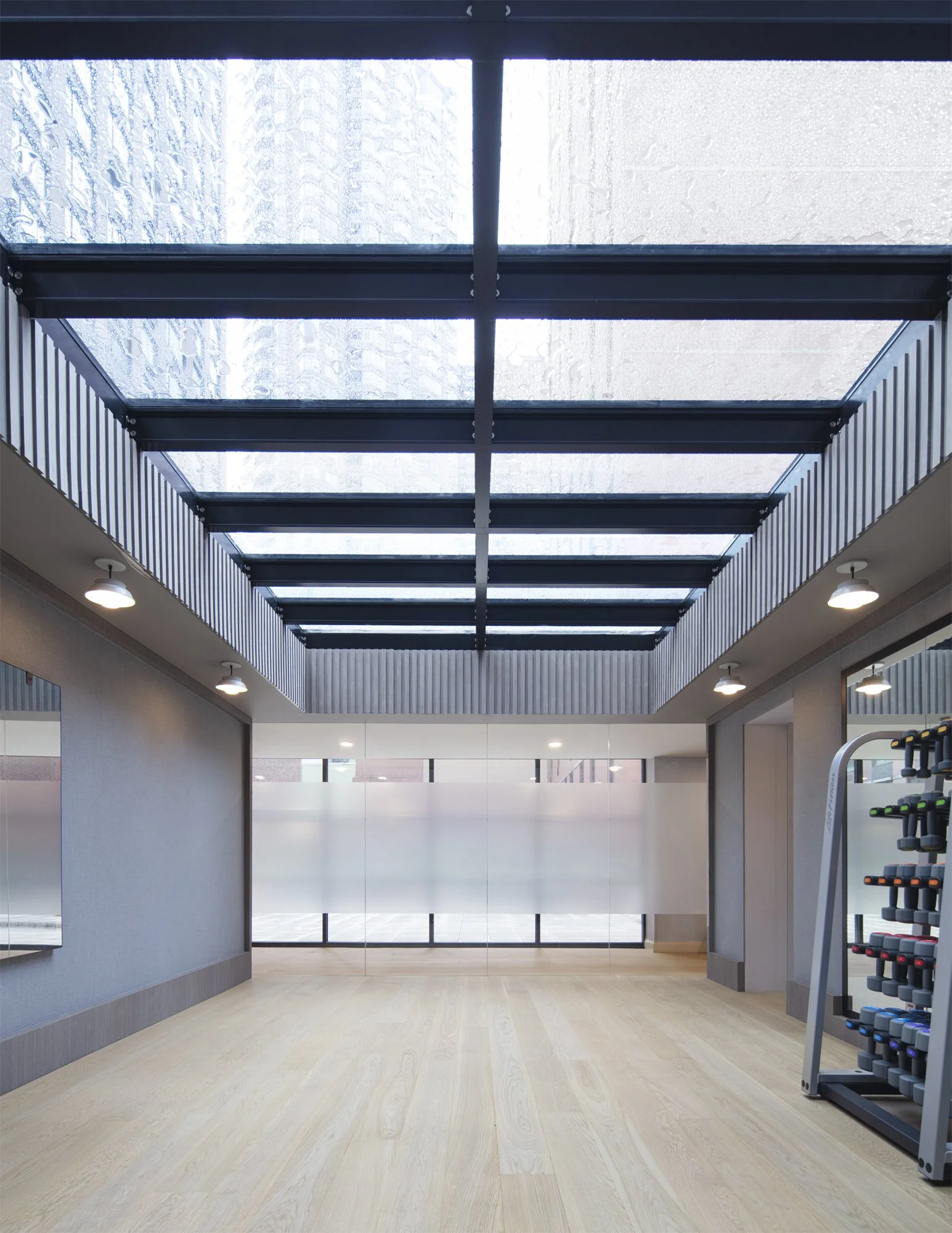JGNA residential fitness studio with a glazed skylight, exposed steel beams, oak floor, and dumbbell rack