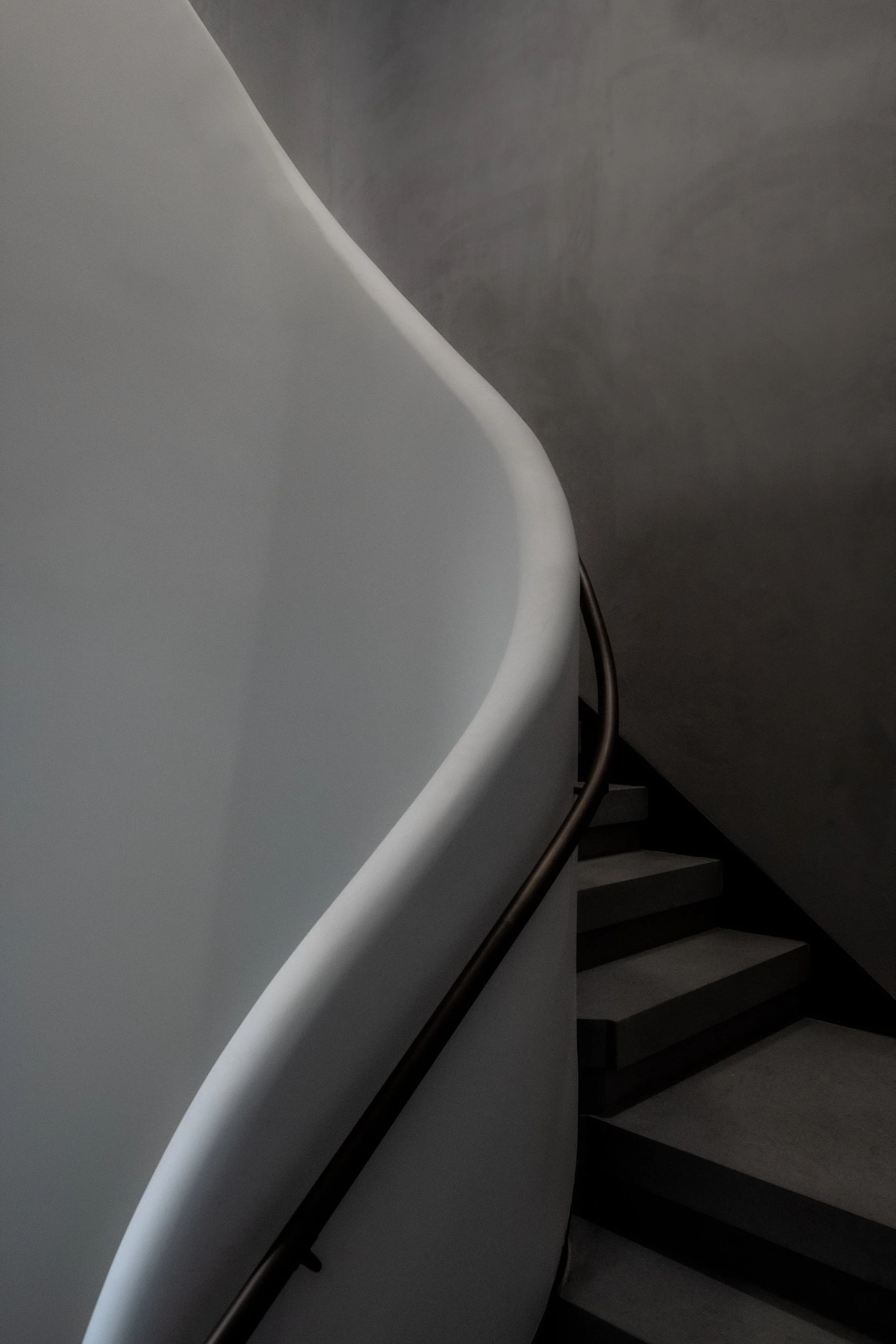 JGNA residential stair detail of a bronze handrail following a sculptural plaster curve