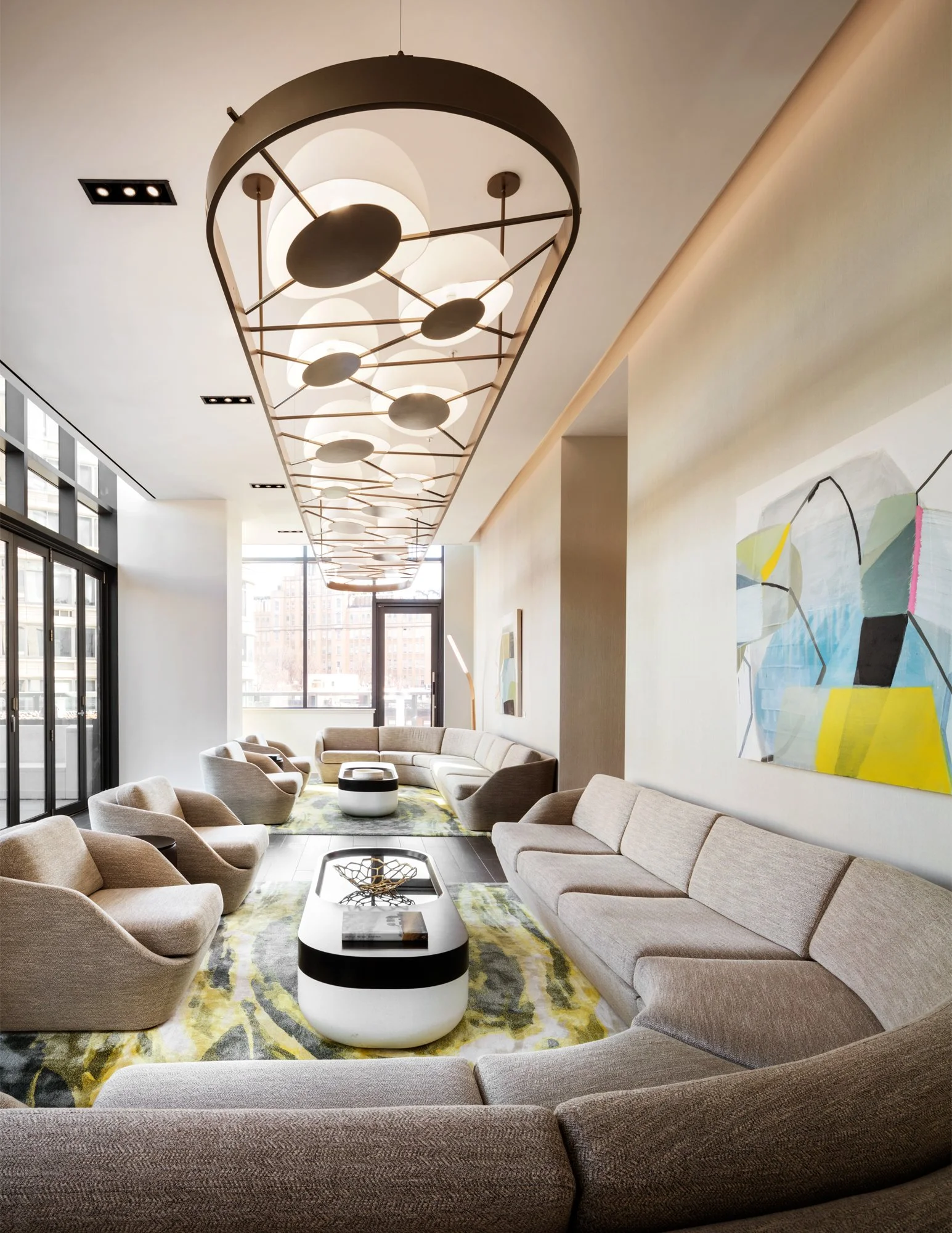 JGNA residential lounge with a curved sectional, a conical wire chandelier, and a large abstract painting