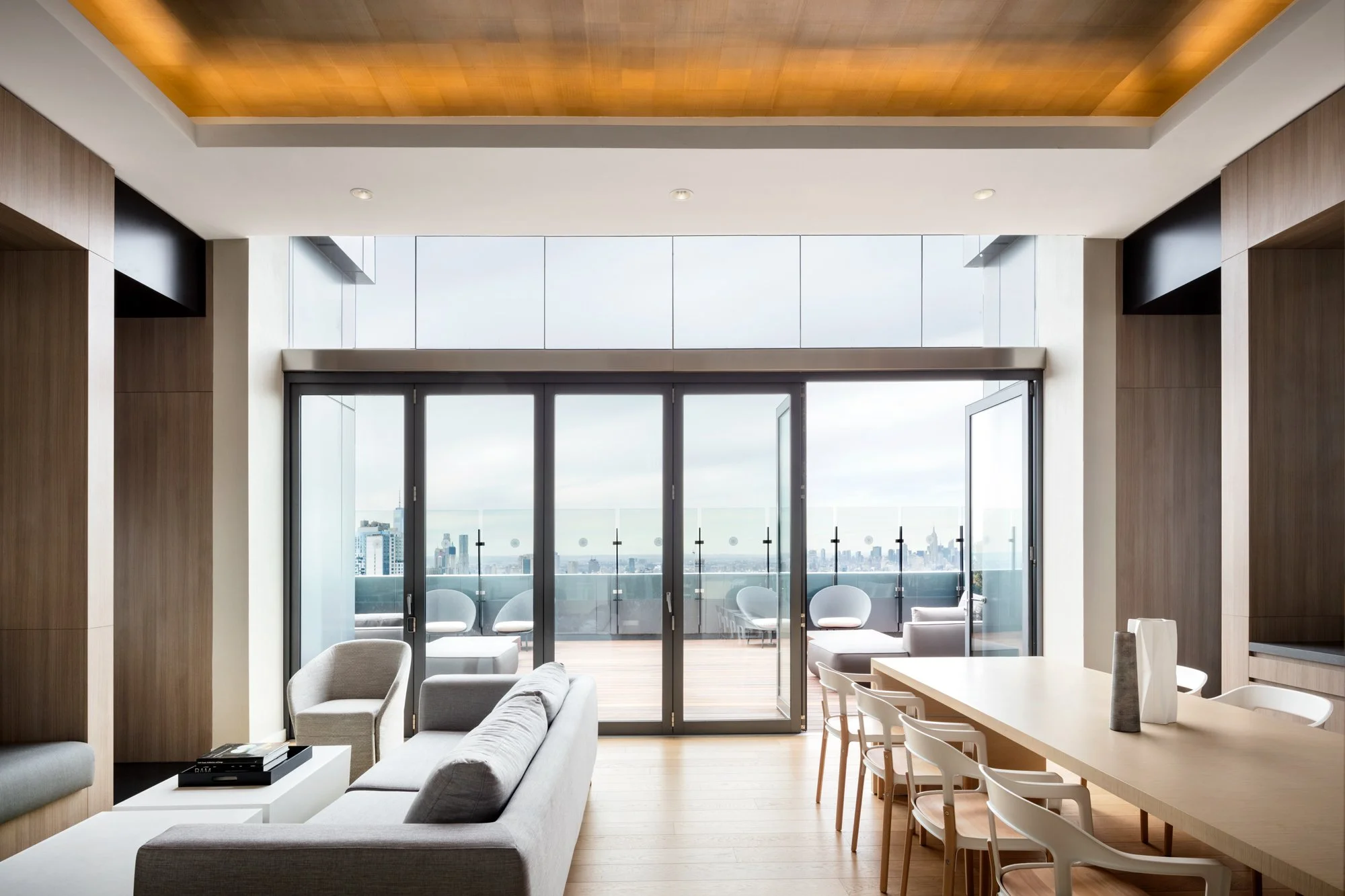 JGNA residential penthouse lounge and dining area with folding glass doors opening to a terrace and skyline