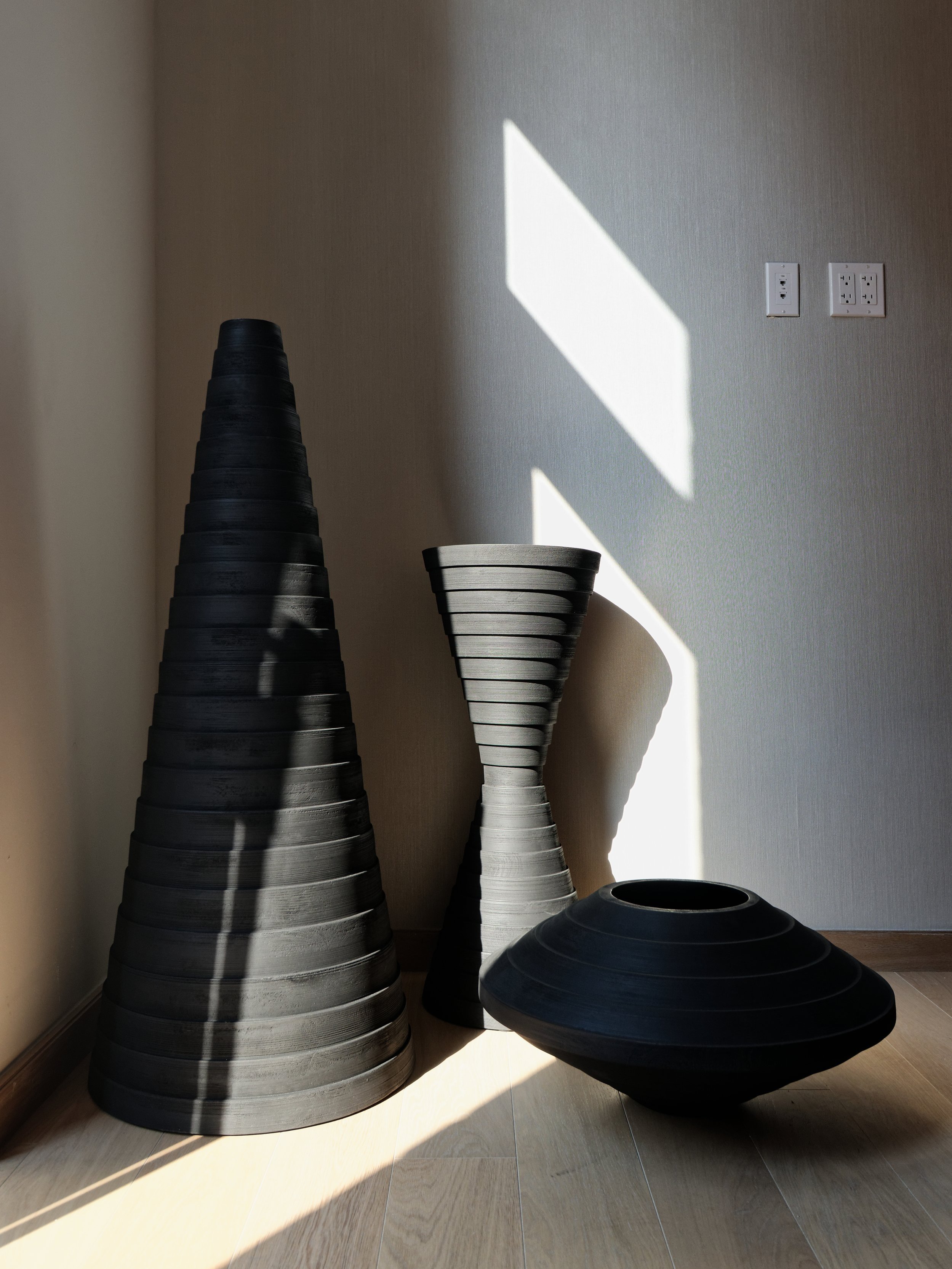 GNA residential detail of a grouping of black and silver ribbed sculptural vessels in sunlight