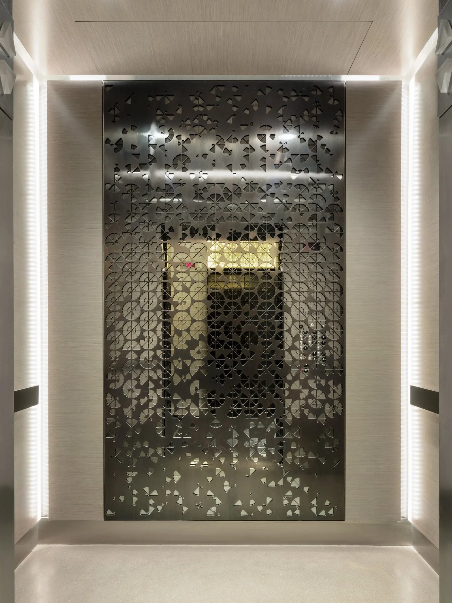 JGNA residential elevator lobby with a perforated metal screen panel and bright cove lighting
