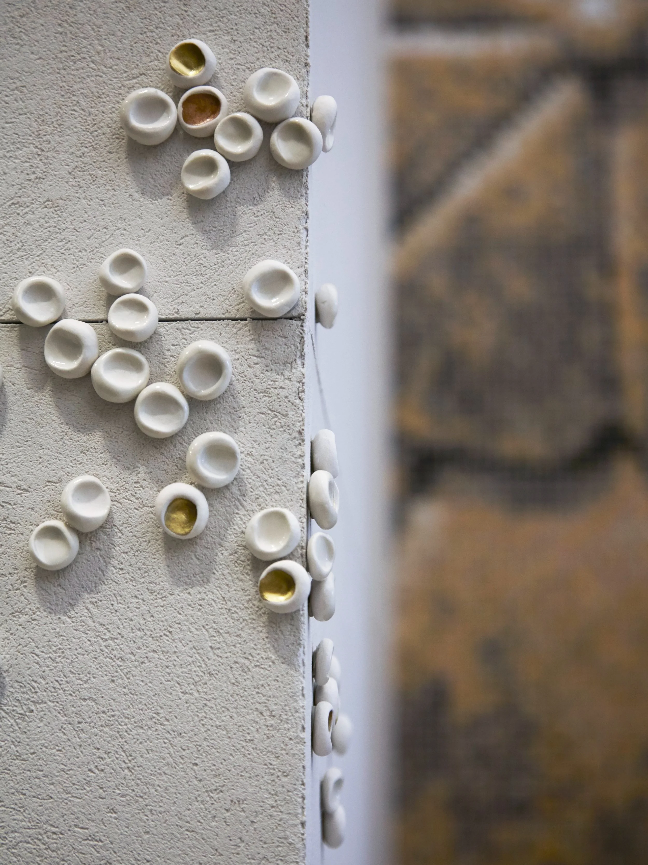 JGNA residential detail of a white and gold ceramic cup wall sculpture on a plaster wall