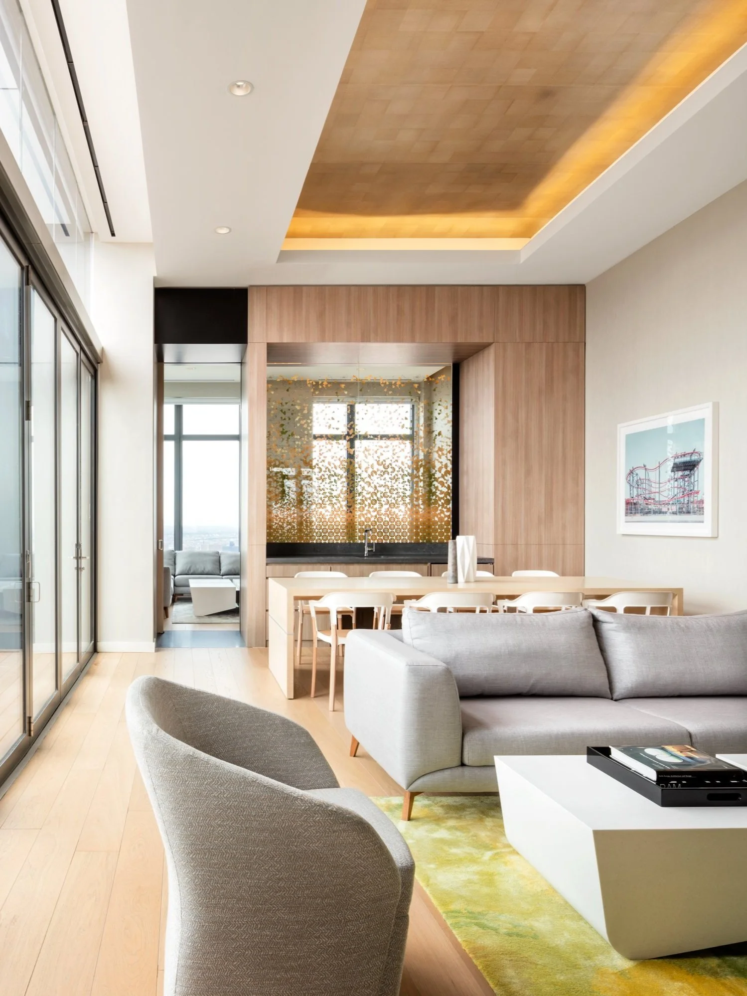 JGNA residential penthouse lounge with a gold-leaf cove ceiling, grey seating, and a private dining room beyond