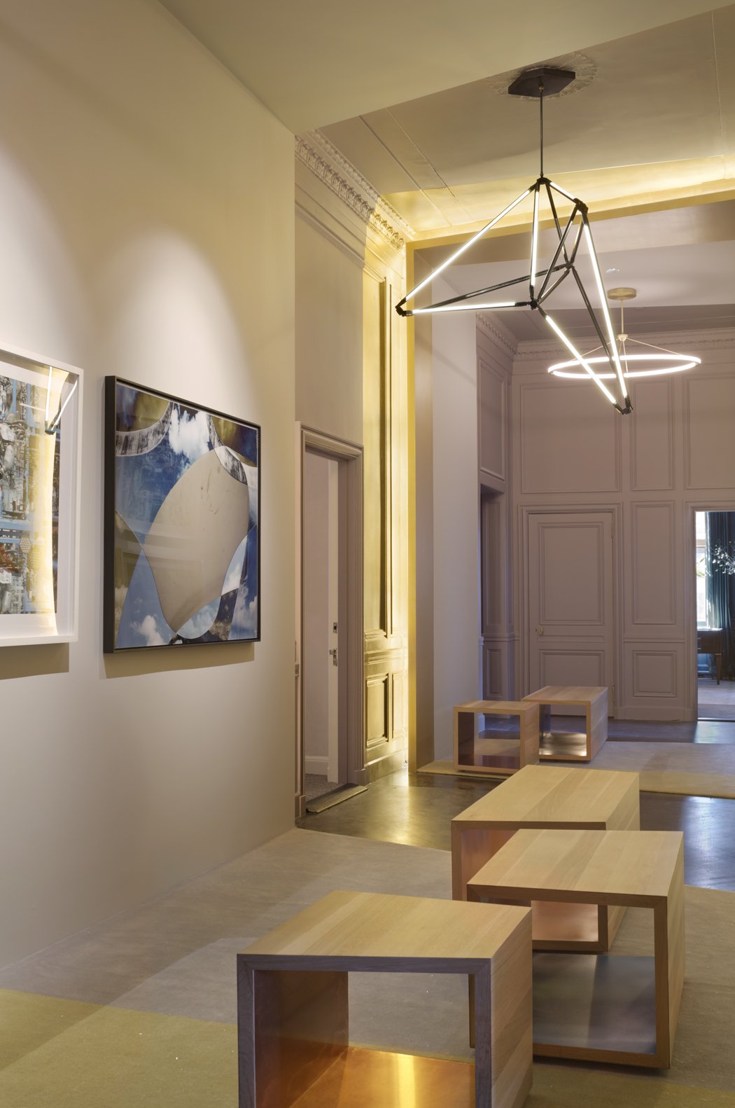 JGNA hallway with a geometric sculptural pendant, low oak bench seating, and framed photographs on paneled walls