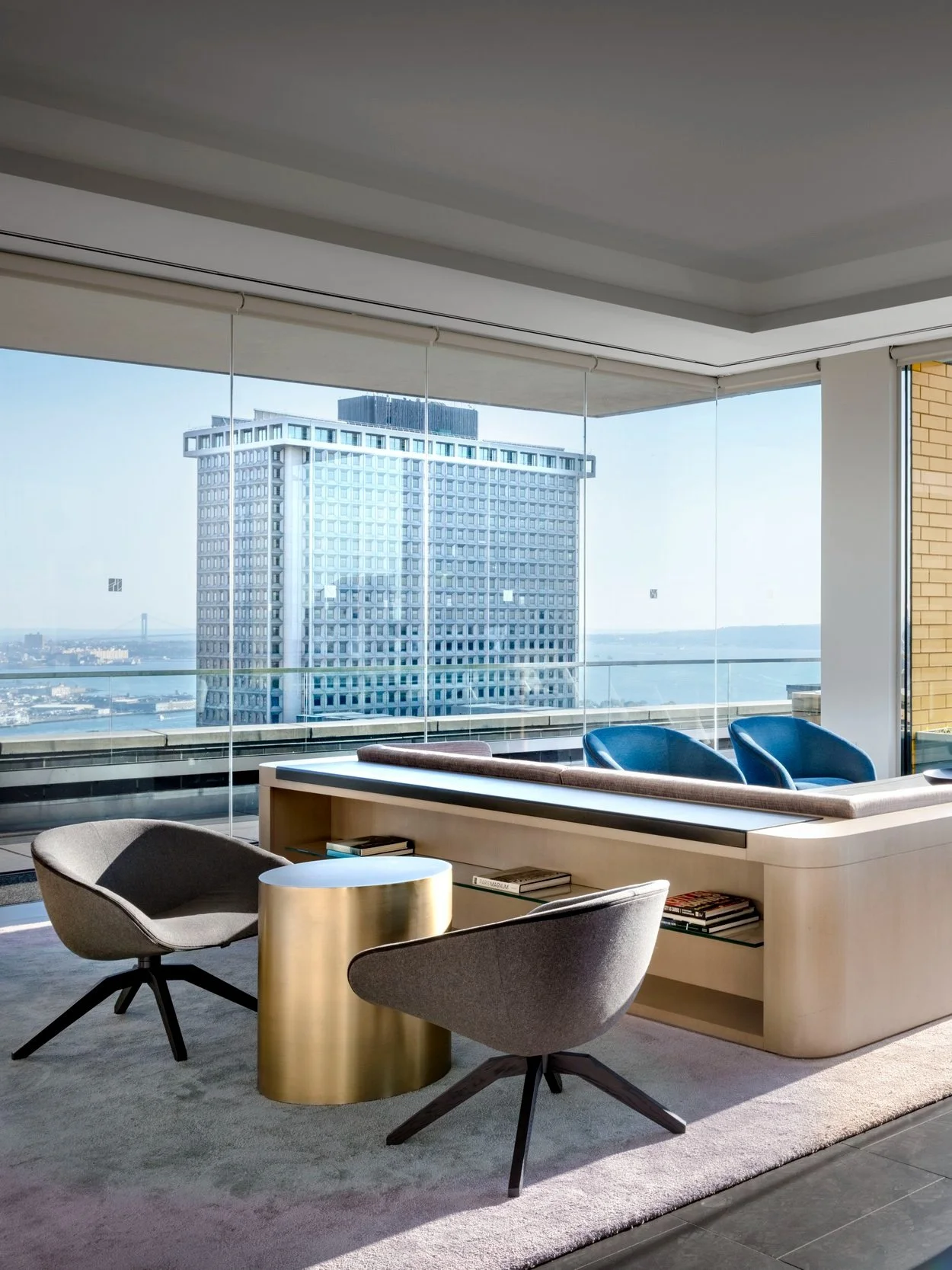 JGNA penthouse seating area with swivel lounge chairs, a brass side table, and a corner window city view